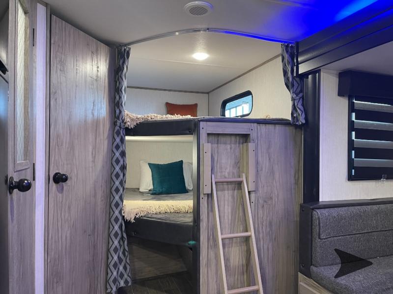 Cozy RV rental interior with wooden bunk beds, a ladder, and a gray seating area, offering comfortable sleeping arrangements.. Forest River Cherokee Alpha Wolf 2022