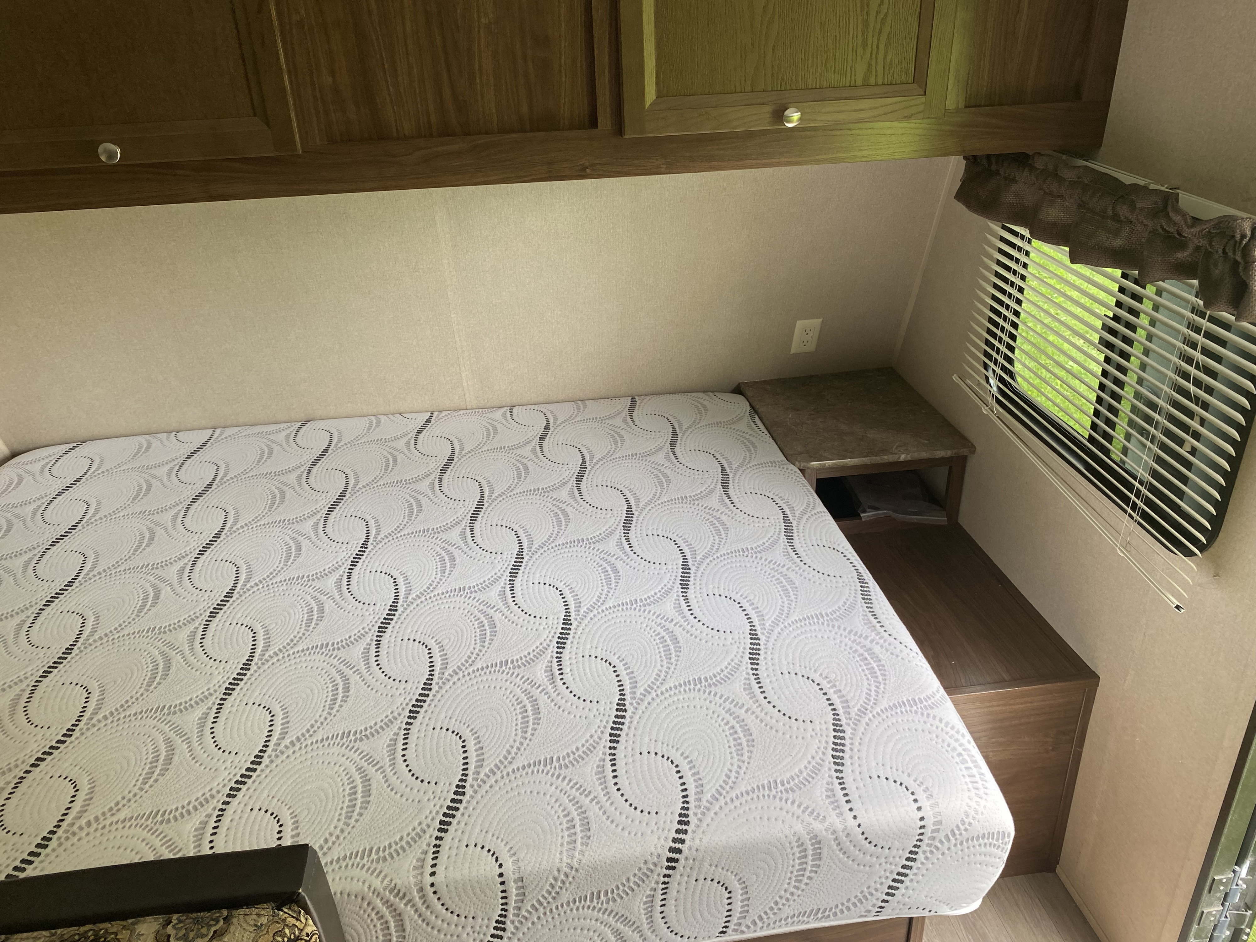Experience an RV rental: a compact sleeping area with a unique patterned mattress, wooden cabinets, and window blinds.. Dutchmen Coleman Lantern 2016