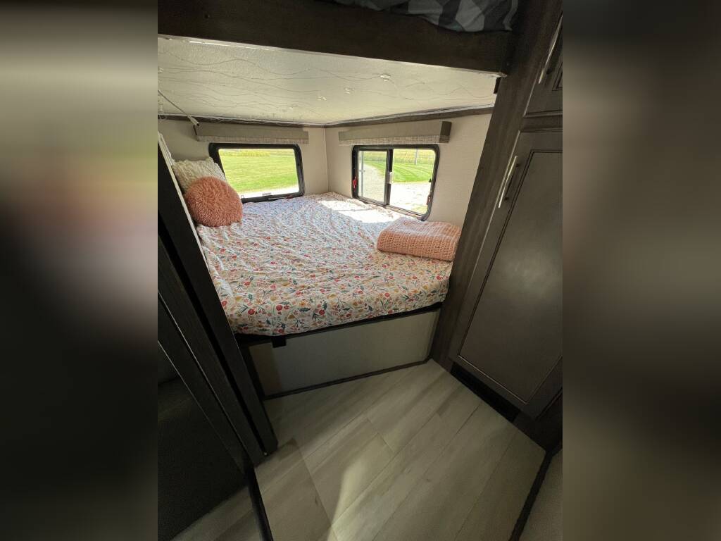 This RV rental bedroom features a comfy bed with floral bedding, a bunk above, and bright windows. Storage closet on right.. Grand Design Solitude 2020