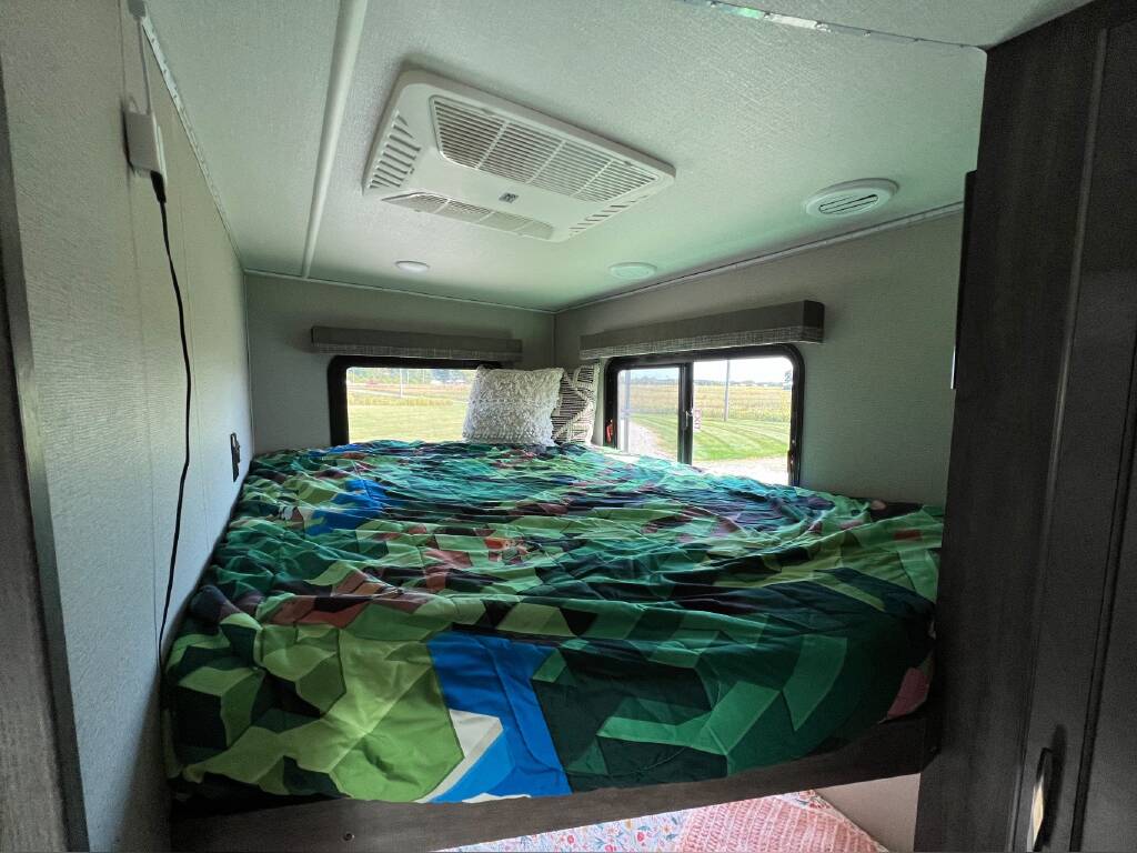 Cozy RV rental bedroom with colorful bedding, AC, and scenic window views.. Grand Design Solitude 2020