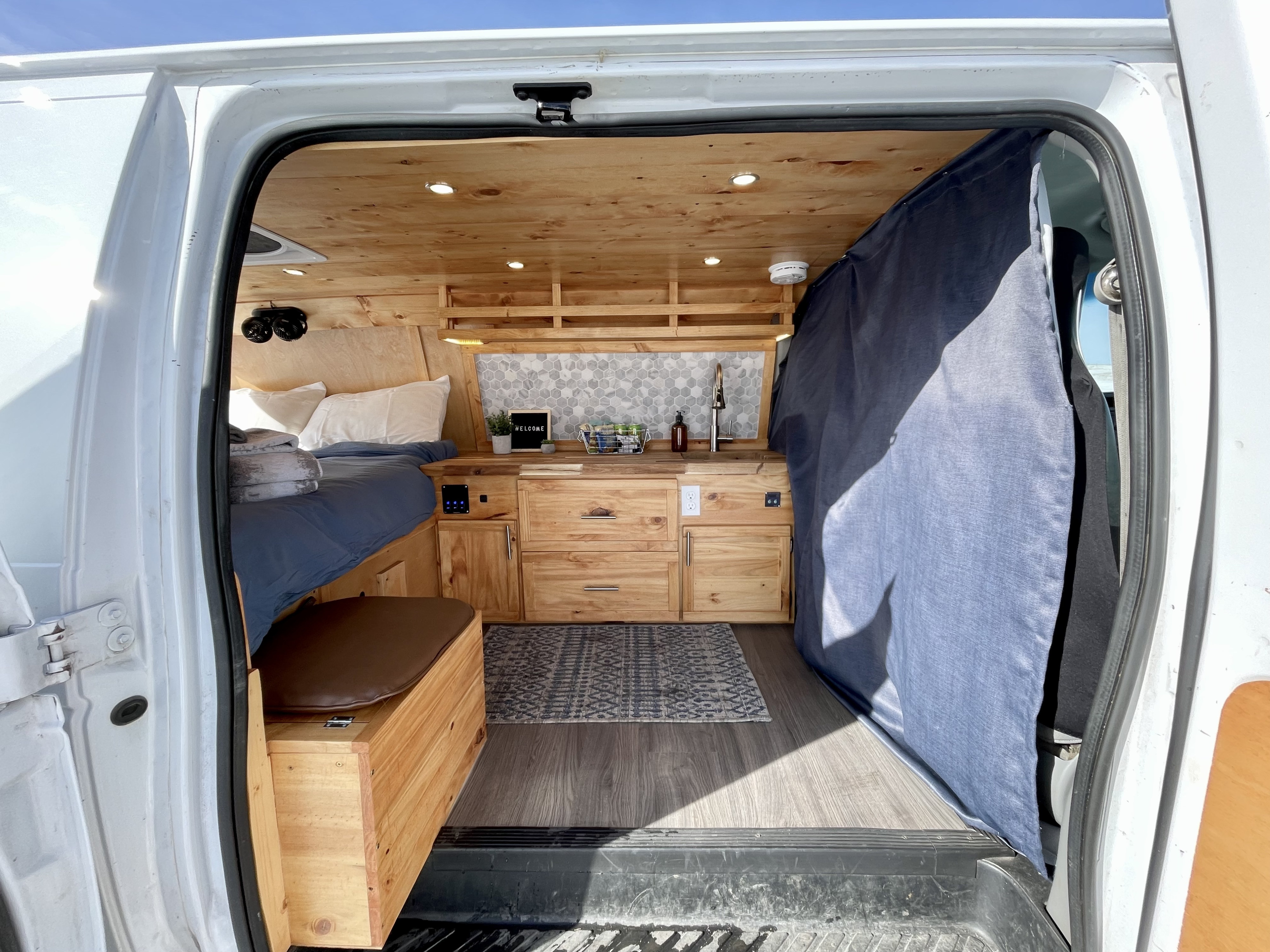 Explore this cozy RV rental's custom-built camper van interior, featuring a bed, wooden kitchen, and living space.. Ford Ford E350 2011