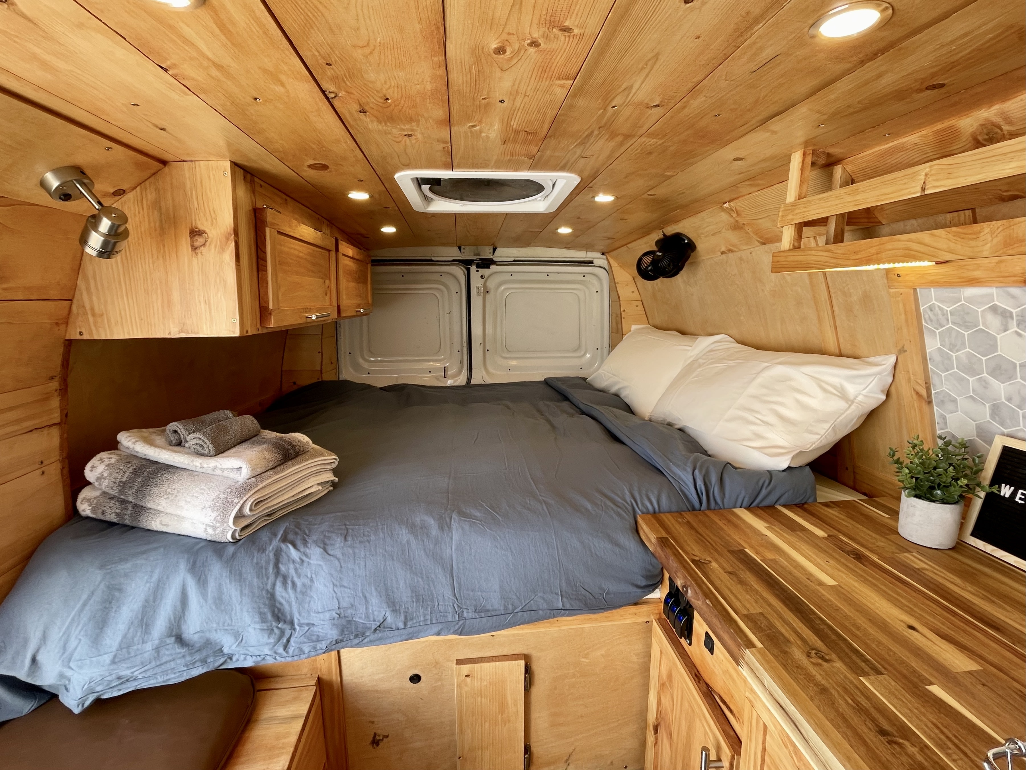 Cozy RV rental interior featuring warm wood paneling, a comfy bed with grey bedding, and clever storage solutions.. Ford Ford E350 2011