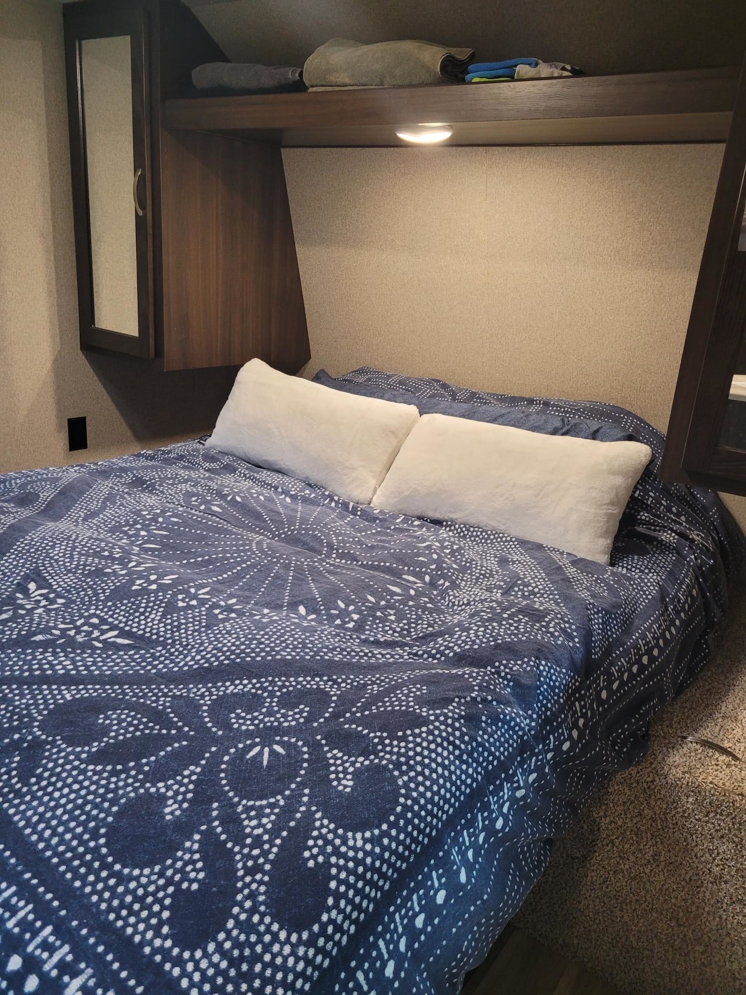 Cozy RV rental bedroom featuring a bed with a blue patterned duvet, white pillows, and overhead cabinets.. Keystone RV Springdale 2020