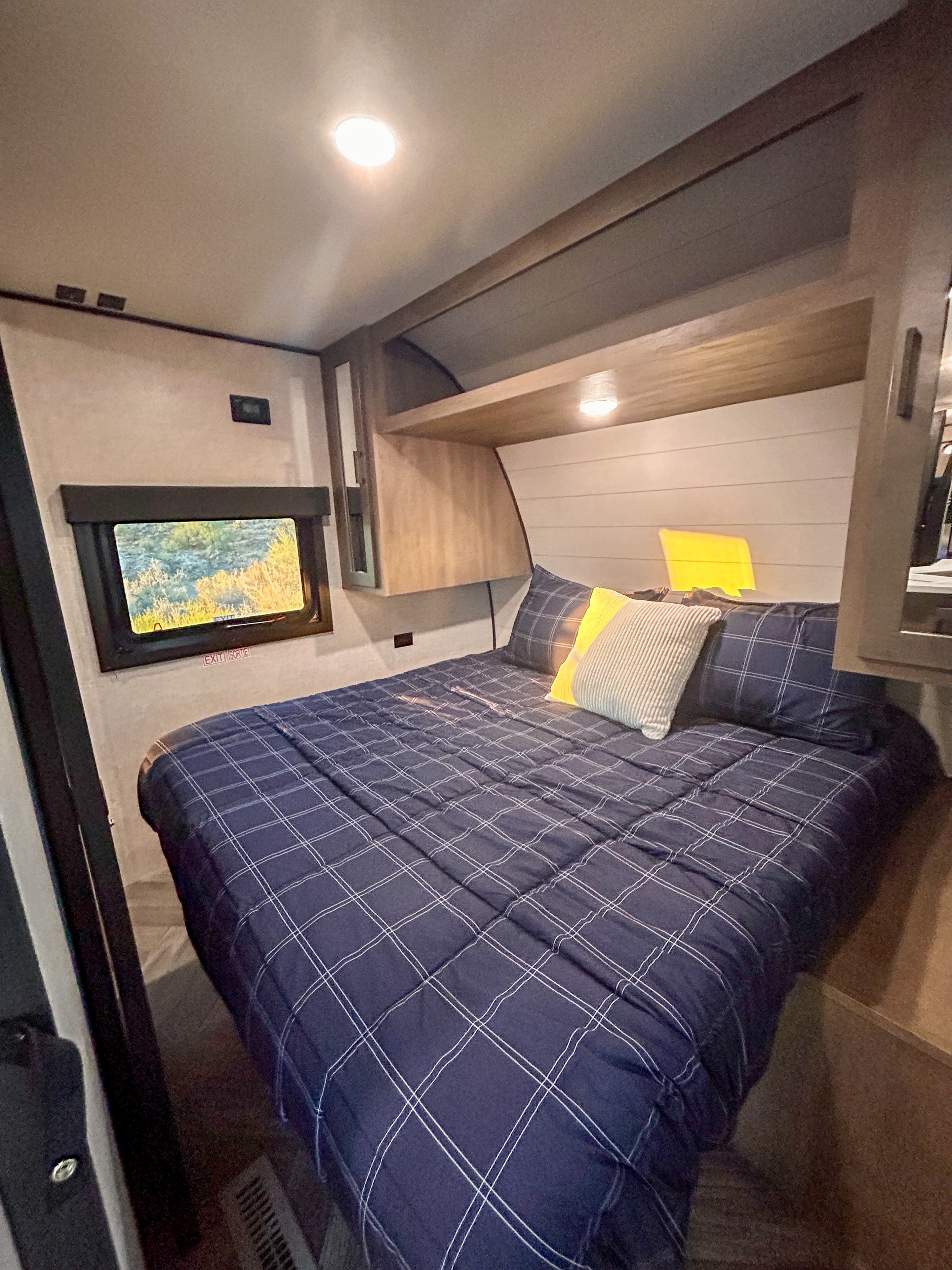 Comfortable RV rental bedroom interior with a cozy bed, plaid comforter, and natural light from the window, perfect for travel.. Starcraft Autumn Ridge 2024