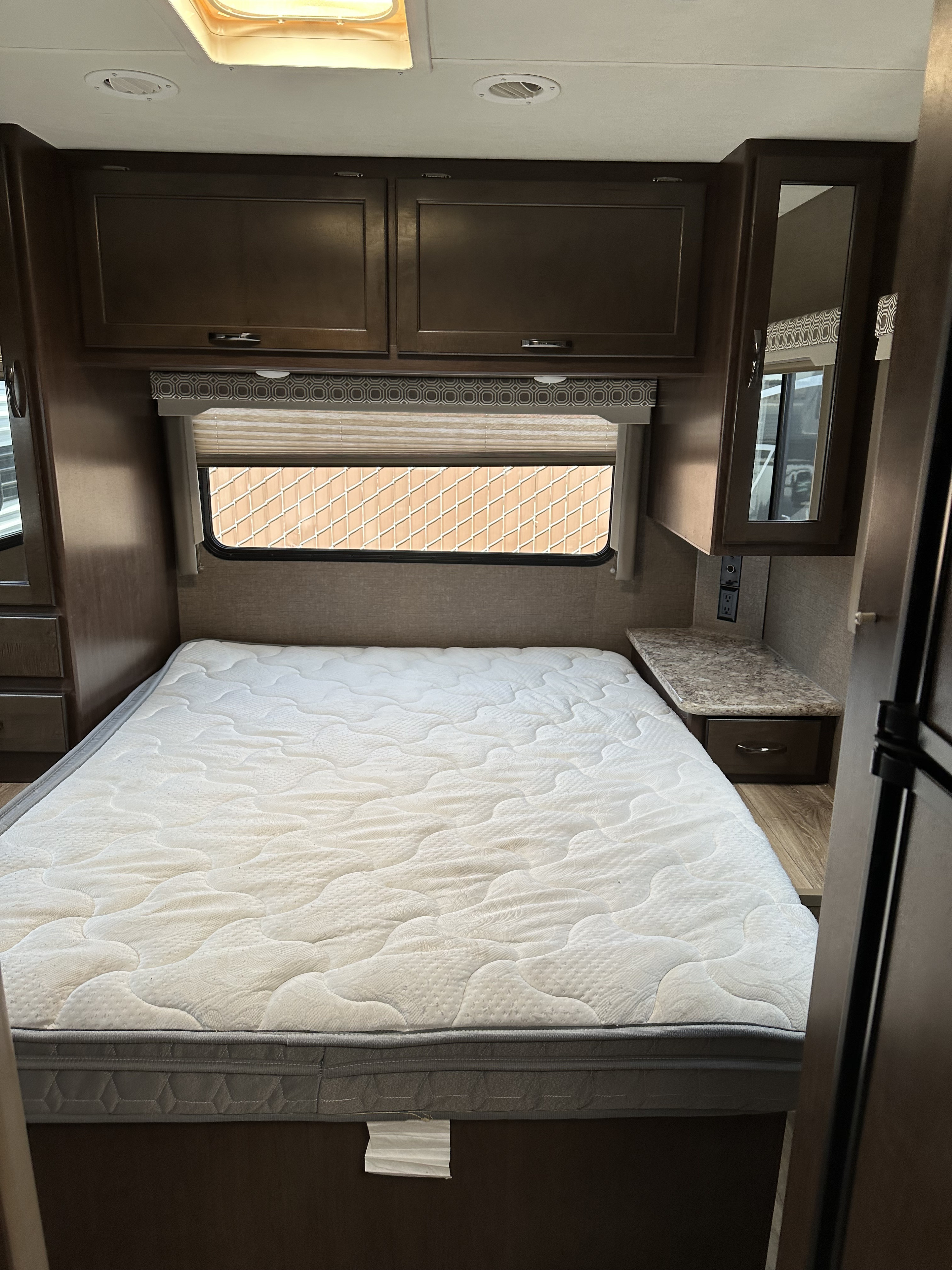 RV rental bedroom: cozy space with white mattress, dark cabinets, window with blinds, and side nightstand.. Thor Motor Coach Four Winds 2020