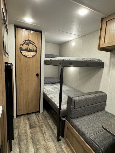 Explore our RV rental's cozy interior: bunk beds, a dinette, and a charming wooden door. Perfect for adventurers.. Forest River Wolf Den 2024