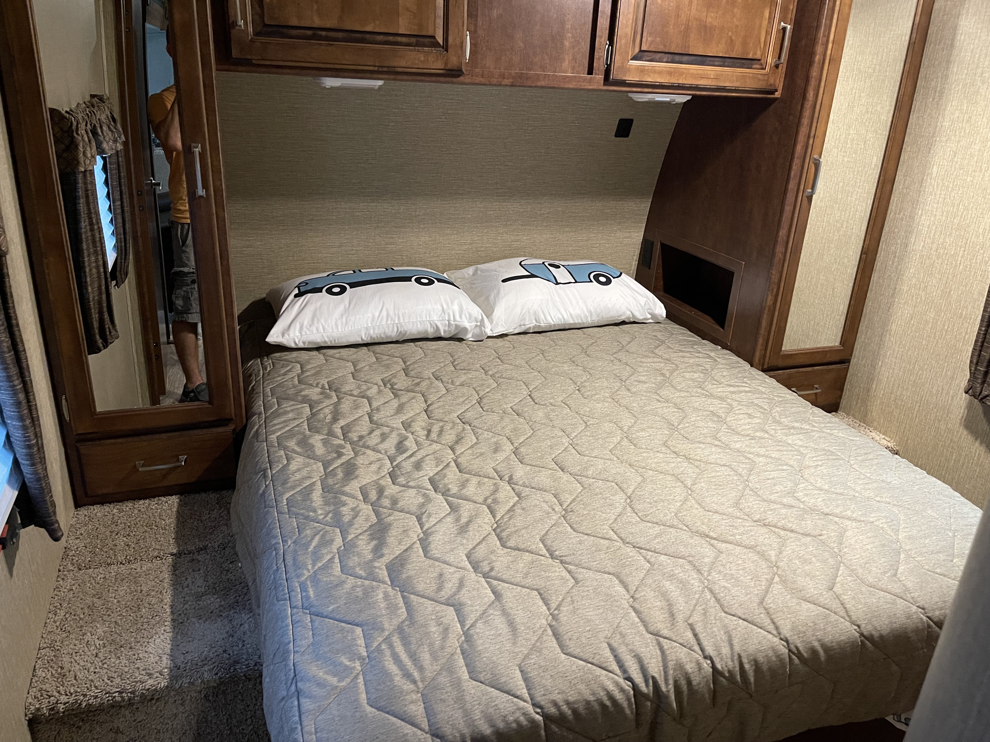 Cozy RV rental bedroom with a quilted bed, fun car pillows, overhead cabinets, and mirrored closets for a compact space.. Keystone RV Outback Super-Lite 2018