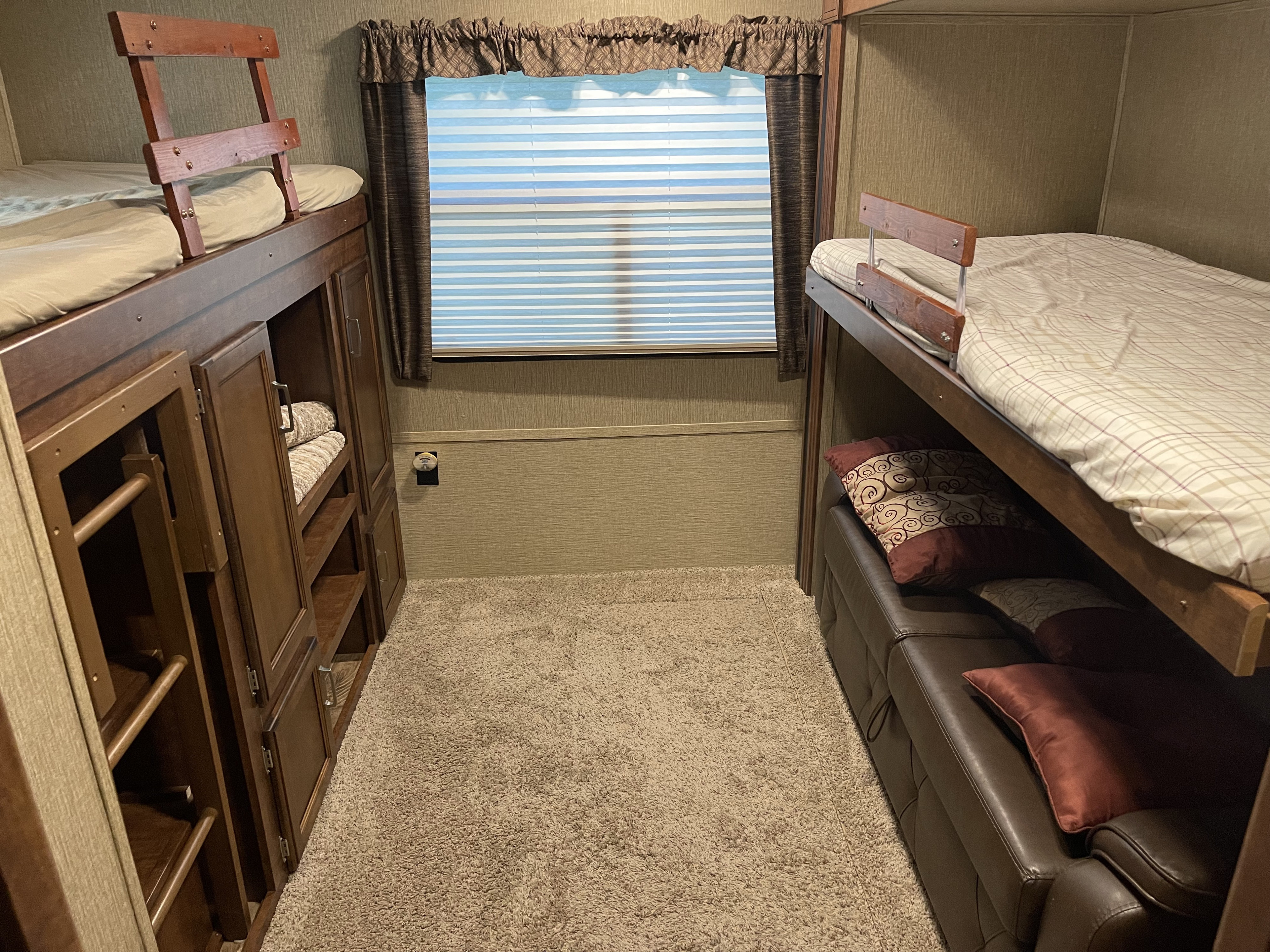An RV rental bedroom featuring left-side bunk beds with storage, right-side bunks above a leather sofa, and a central window.. Keystone RV Outback Super-Lite 2018
