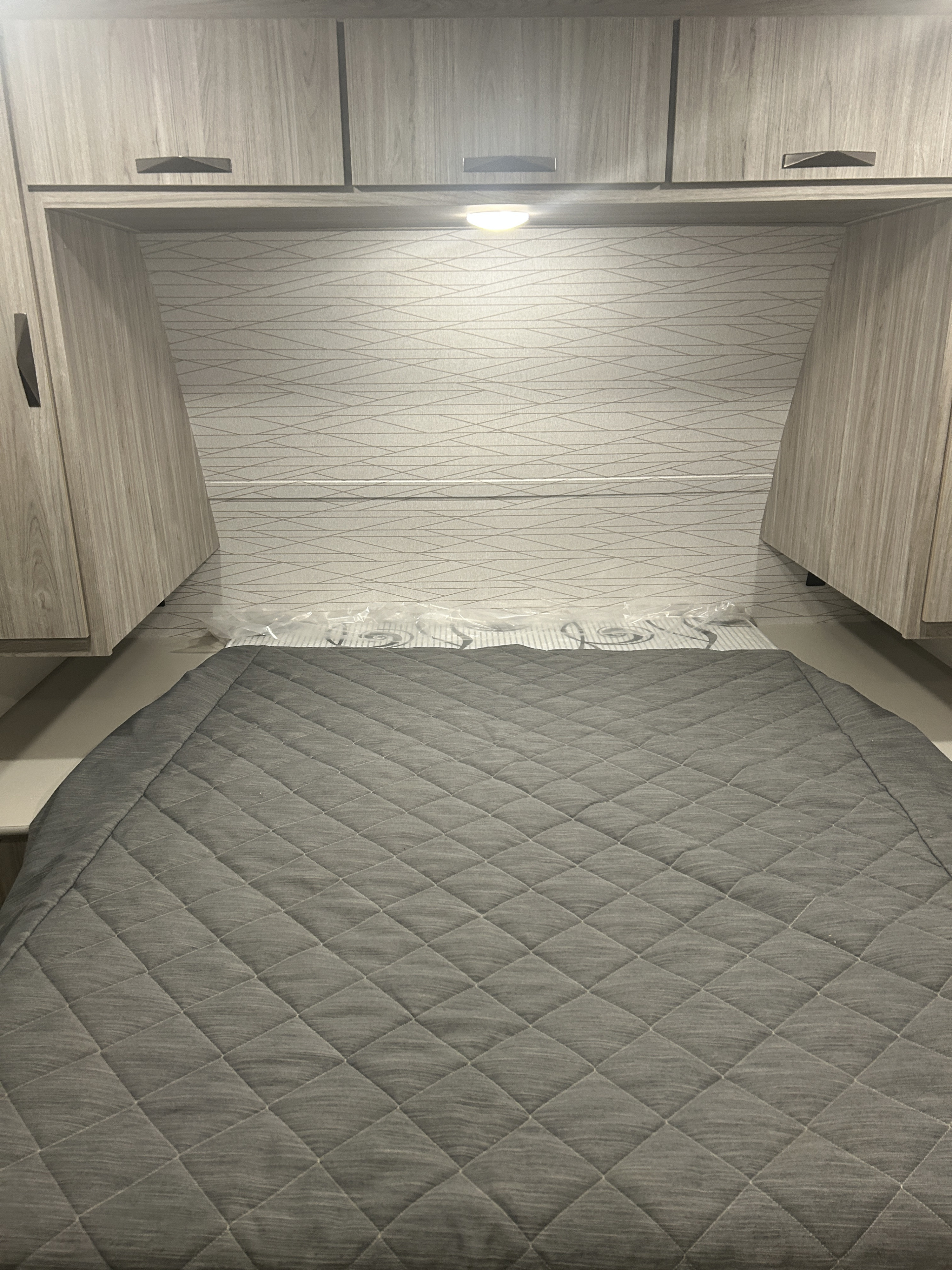 RV rental bedroom: a cozy interior with a gray quilted bed, light wood cabinets, patterned headboard, and reading light.. Keystone RV 229bh/we 2024