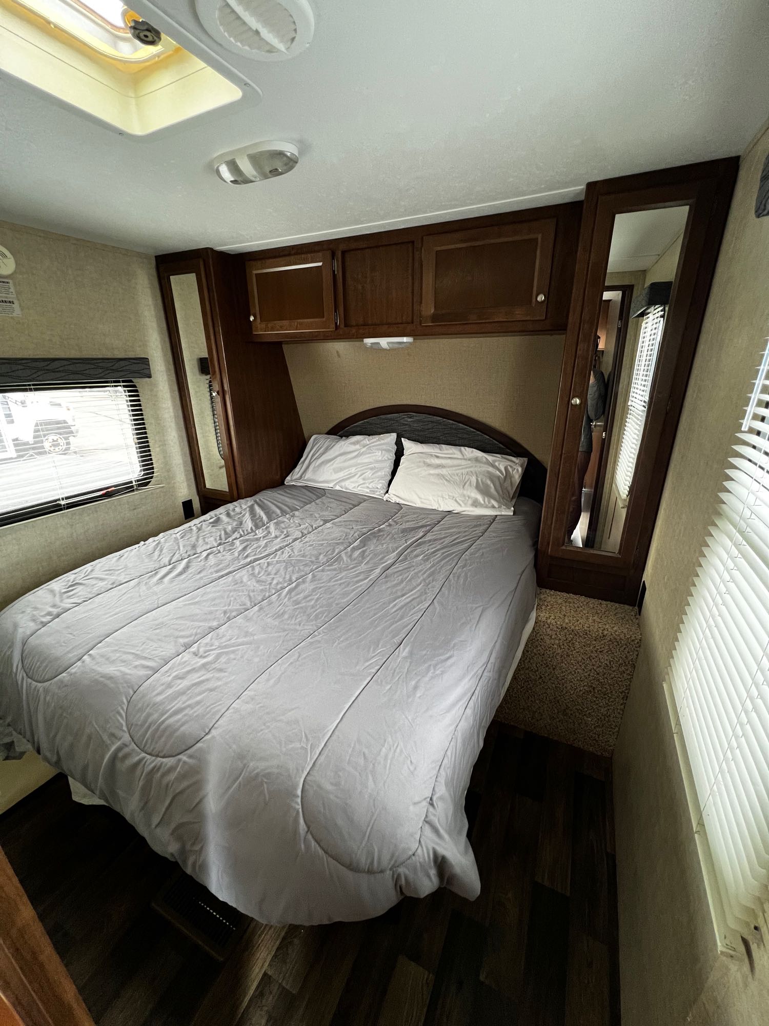 Comfortable RV rental bedroom with a grey bed, wooden cabinets, and mirrors, brightened by windows and a skylight.. Keystone RV Hideout 2015