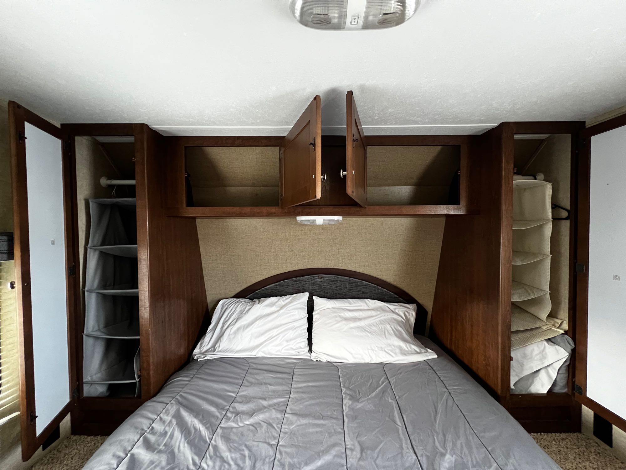 An RV rental bedroom with a bed, open overhead cabinets, and side closets. Compact and practical.. Keystone RV Hideout 2015