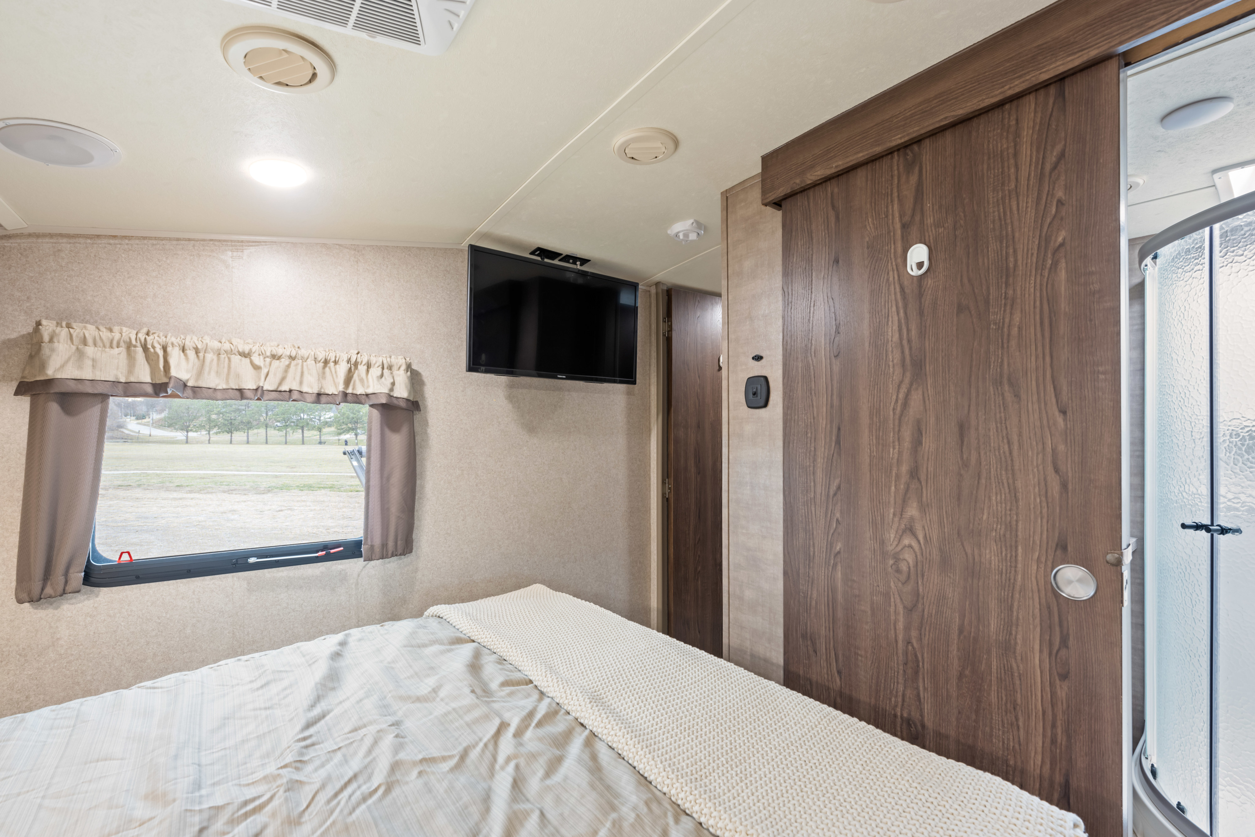 Inside an RV rental: a bedroom with a comfortable bed, wall-mounted TV, window overlooking nature, and a shower nearby.. Forest River Signiture Ultra Lite 2017