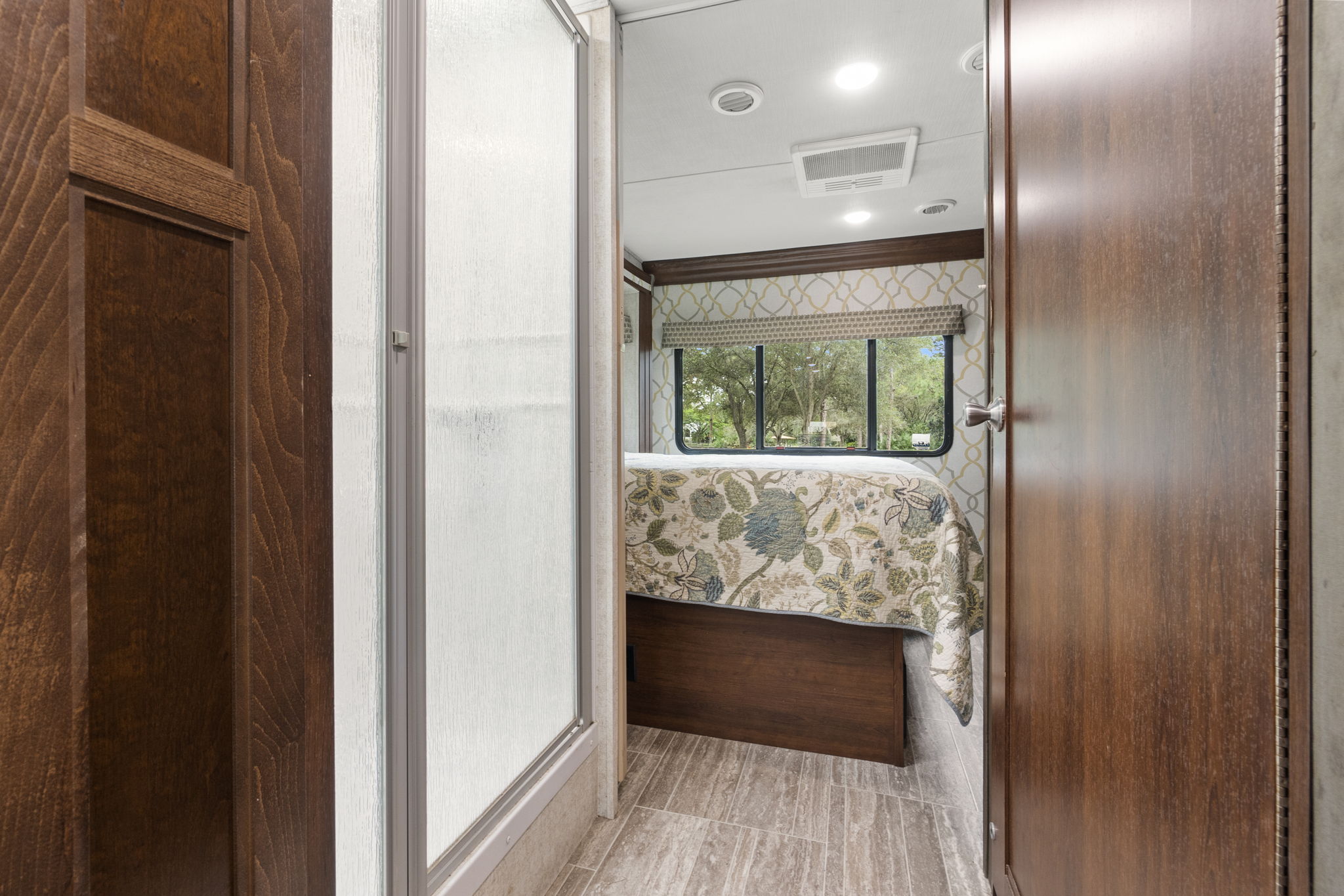 Cozy RV rental bedroom view from the hallway, featuring a patterned bed, large window, and part of the shower.. Forest River Sunseeker Classic 2021