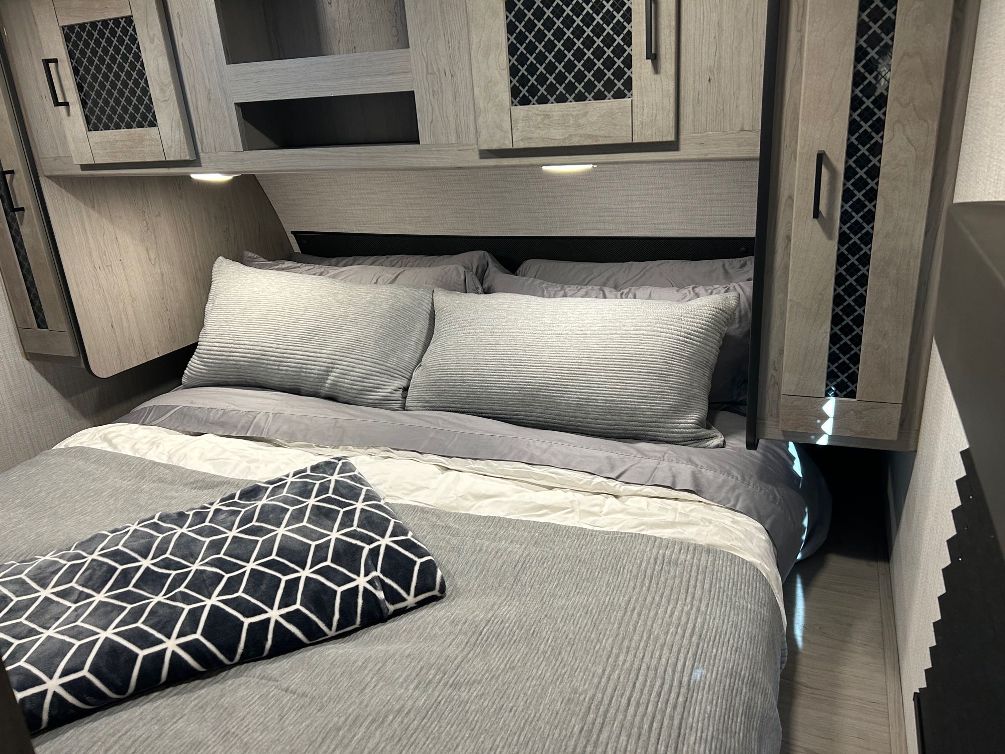 Cozy gray bedroom in an RV rental, featuring overhead cabinets, soft bedding, and integrated lighting. Ideal for travel.. Heartland RVs Mallard 2021