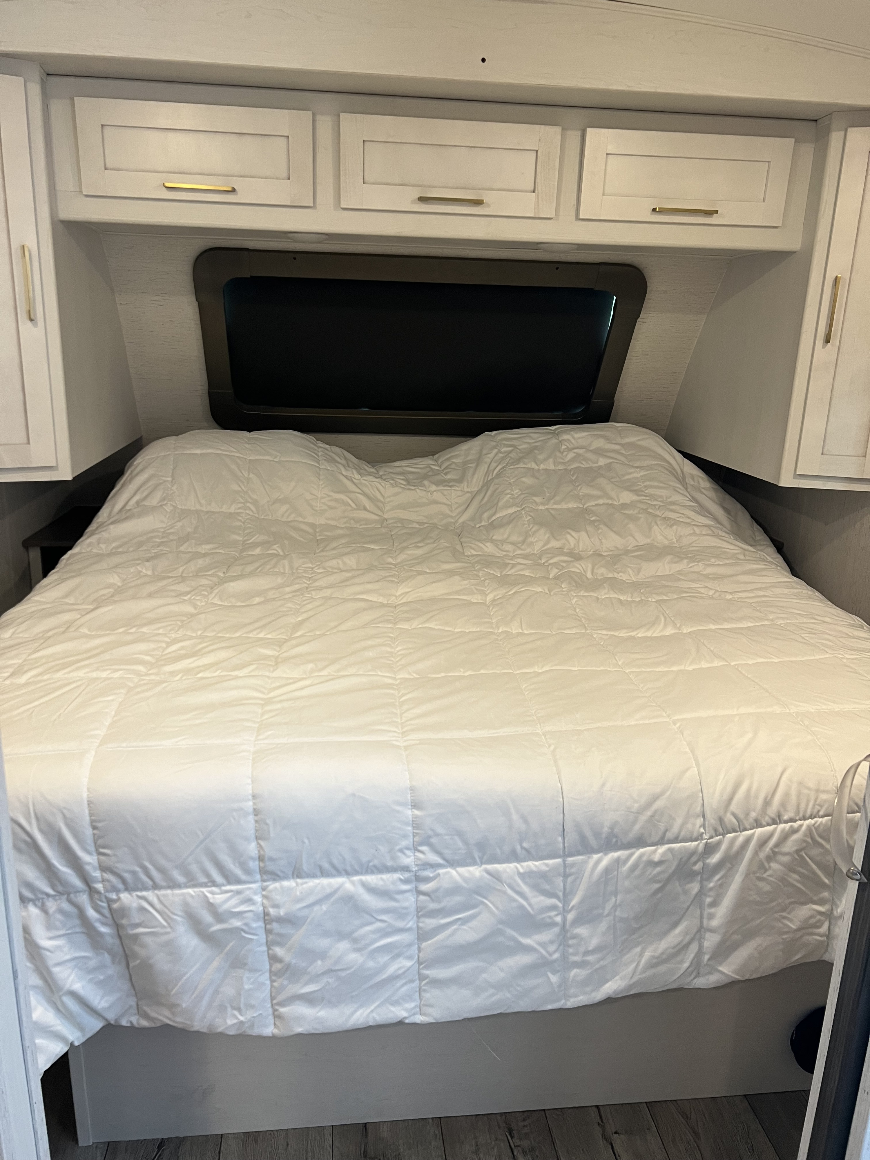 Cozy RV rental bedroom with a white comforter bed, overhead cabinets, and a large window.. Keystone RV Astoria 2903BH 2022