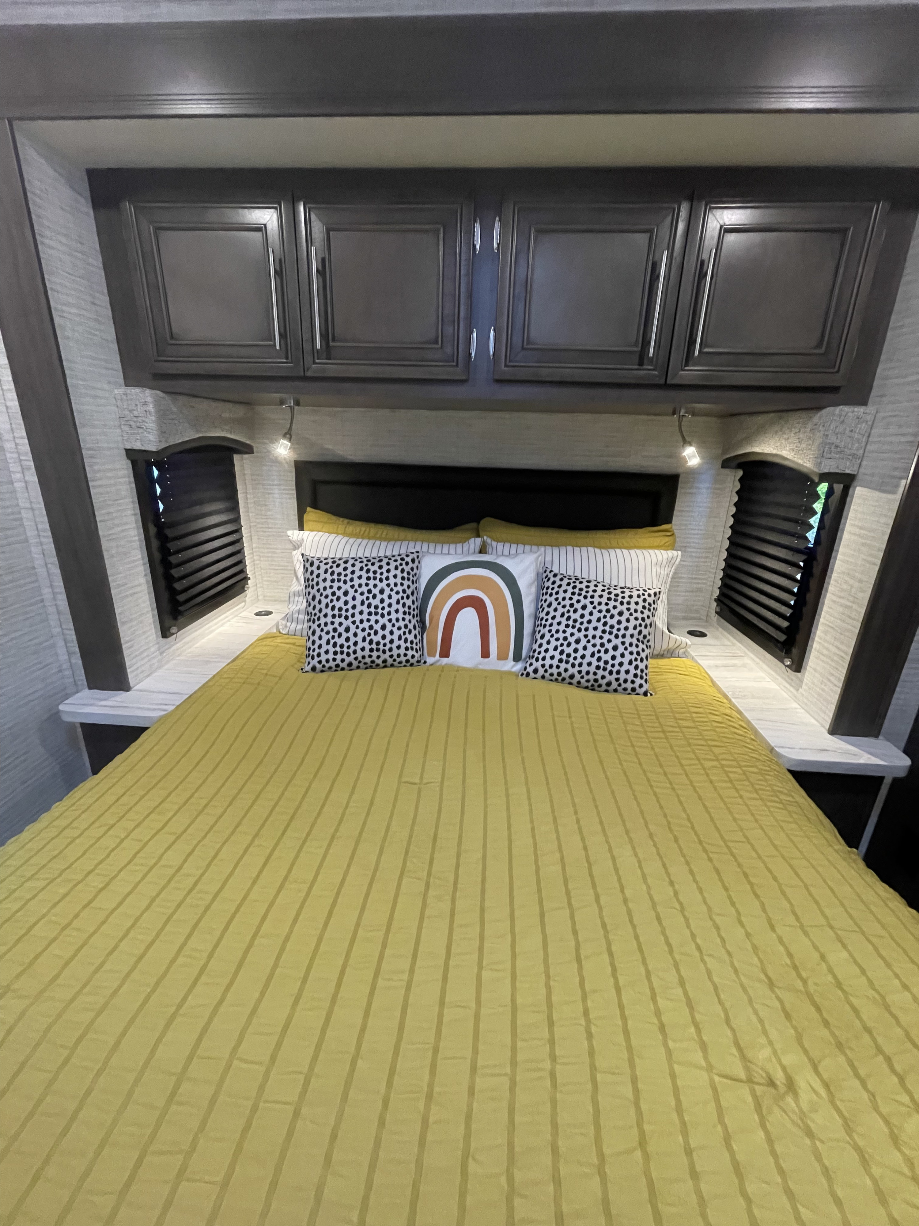 Cozy RV rental bedroom featuring a bright yellow bed, accent pillows, and dark modern cabinets for comfortable travel.. Entegra Coach Odyssey 2024