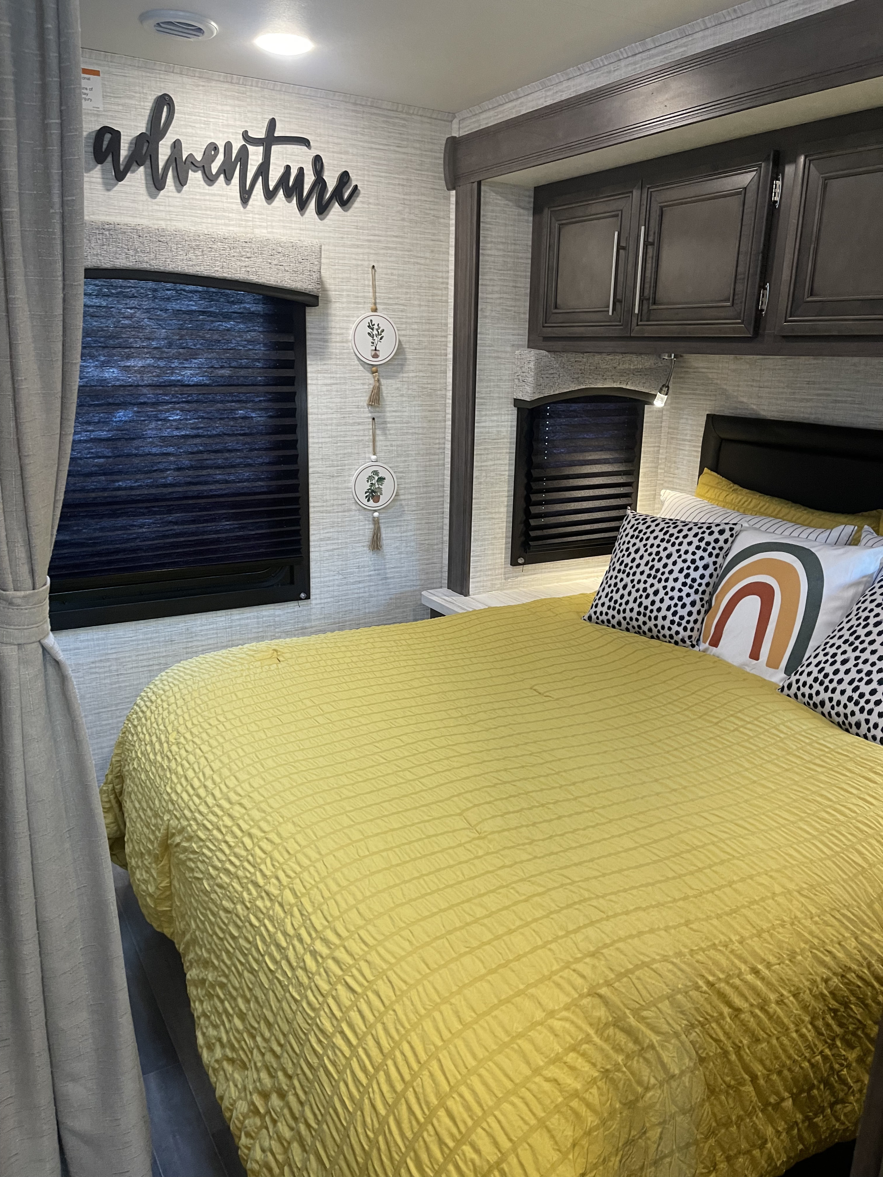 Experience comfort in this cozy RV rental bedroom. Features a yellow bed, adventure sign, and built-in storage.. Entegra Coach Odyssey 2024