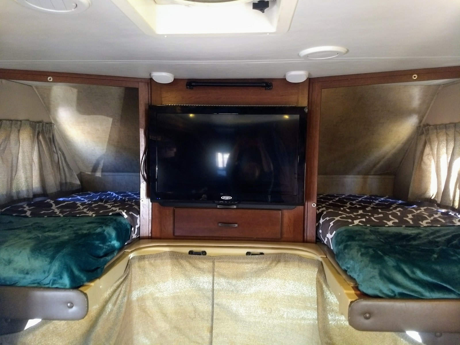 Cozy RV rental interior: two beds with patterned bedding and green blankets, plus a central TV.. Forest River forester 2016