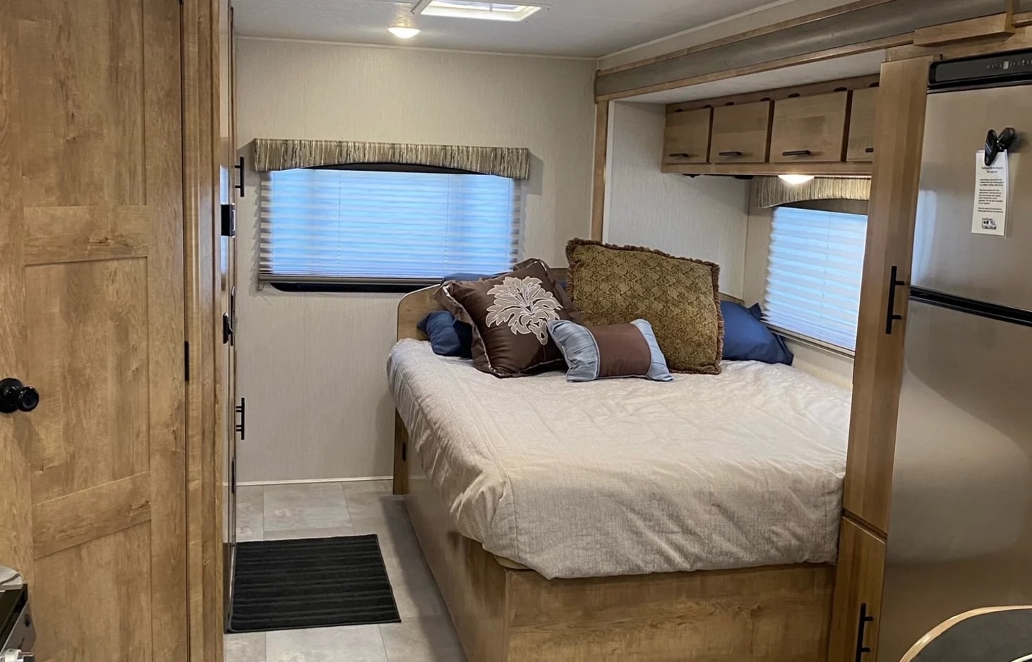 Cozy RV rental bedroom featuring a large bed with decorative pillows, a window, and overhead storage cabinets.. Forest River Coachmen Leprechaun 2020