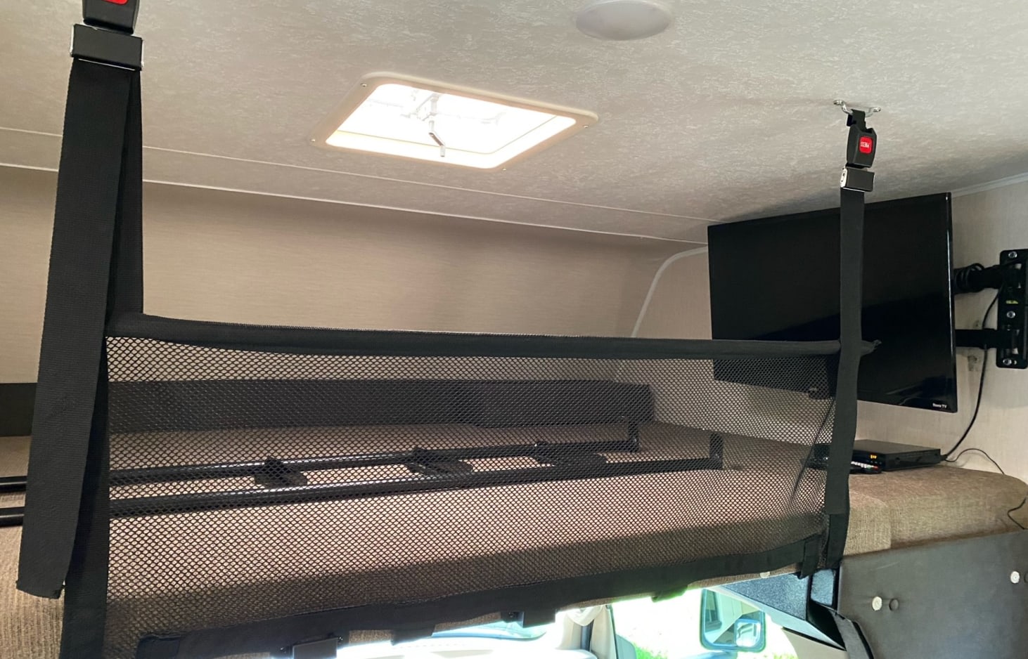 Overhead bunk with mesh safety net secured to ceiling via straps, visible TV and entertainment system in an RV rental.. Forest River Coachmen Leprechaun 2020
