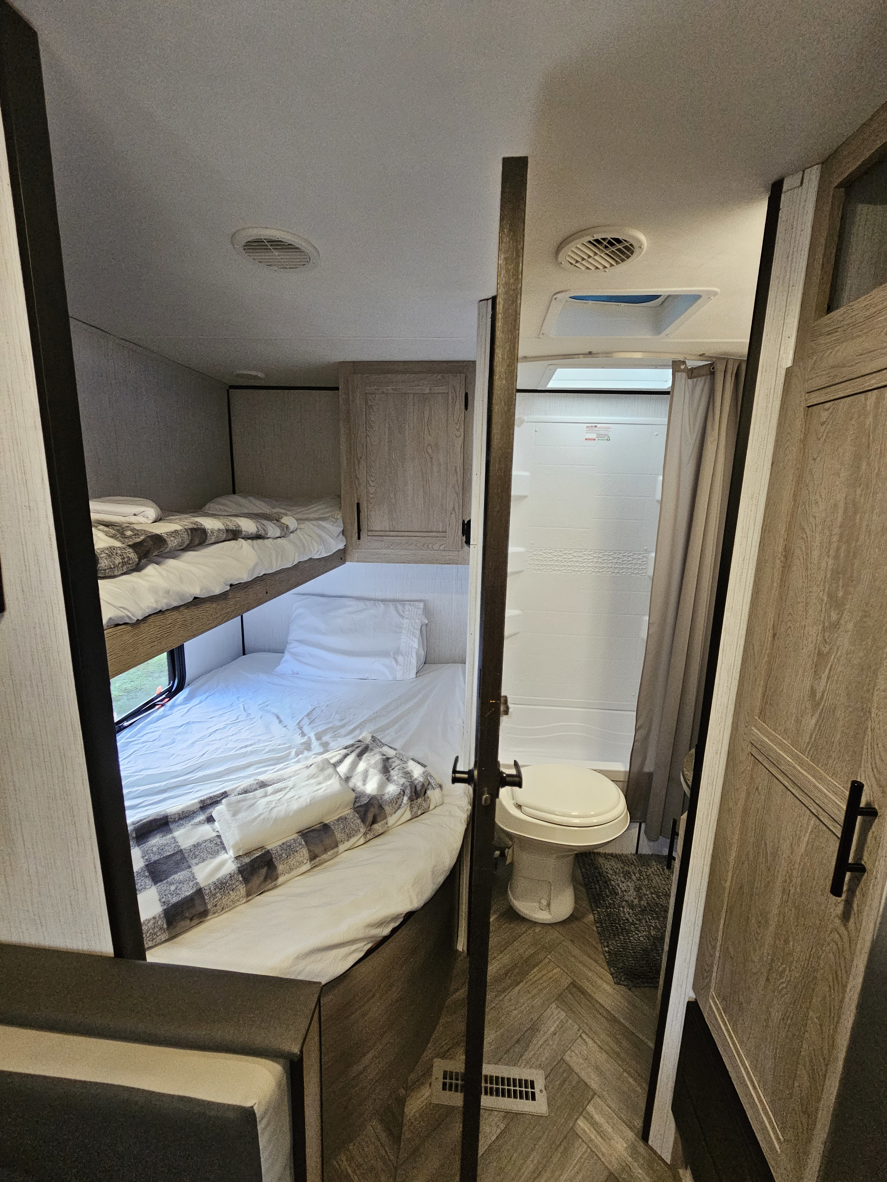 This RV rental showcases its sleeping and bathroom areas. On the left are two bunk beds; on the right, a compact bathroom with toilet.. Keystone Prowler 2021