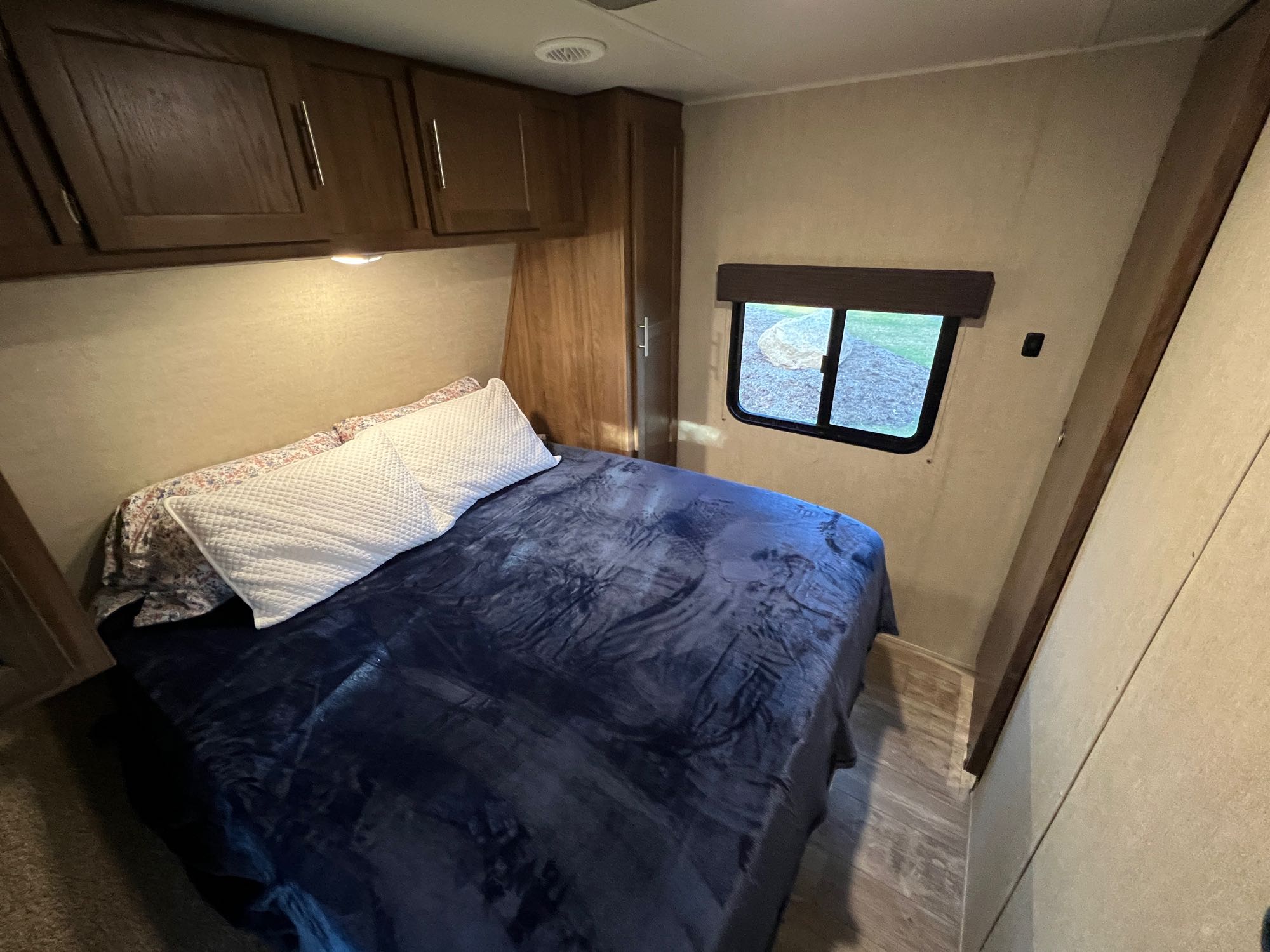 Cozy RV rental bedroom with a comfortable bed, soft blue blanket, overhead cabinets, and a window revealing nature.. Gulf Stream Conquest 2019