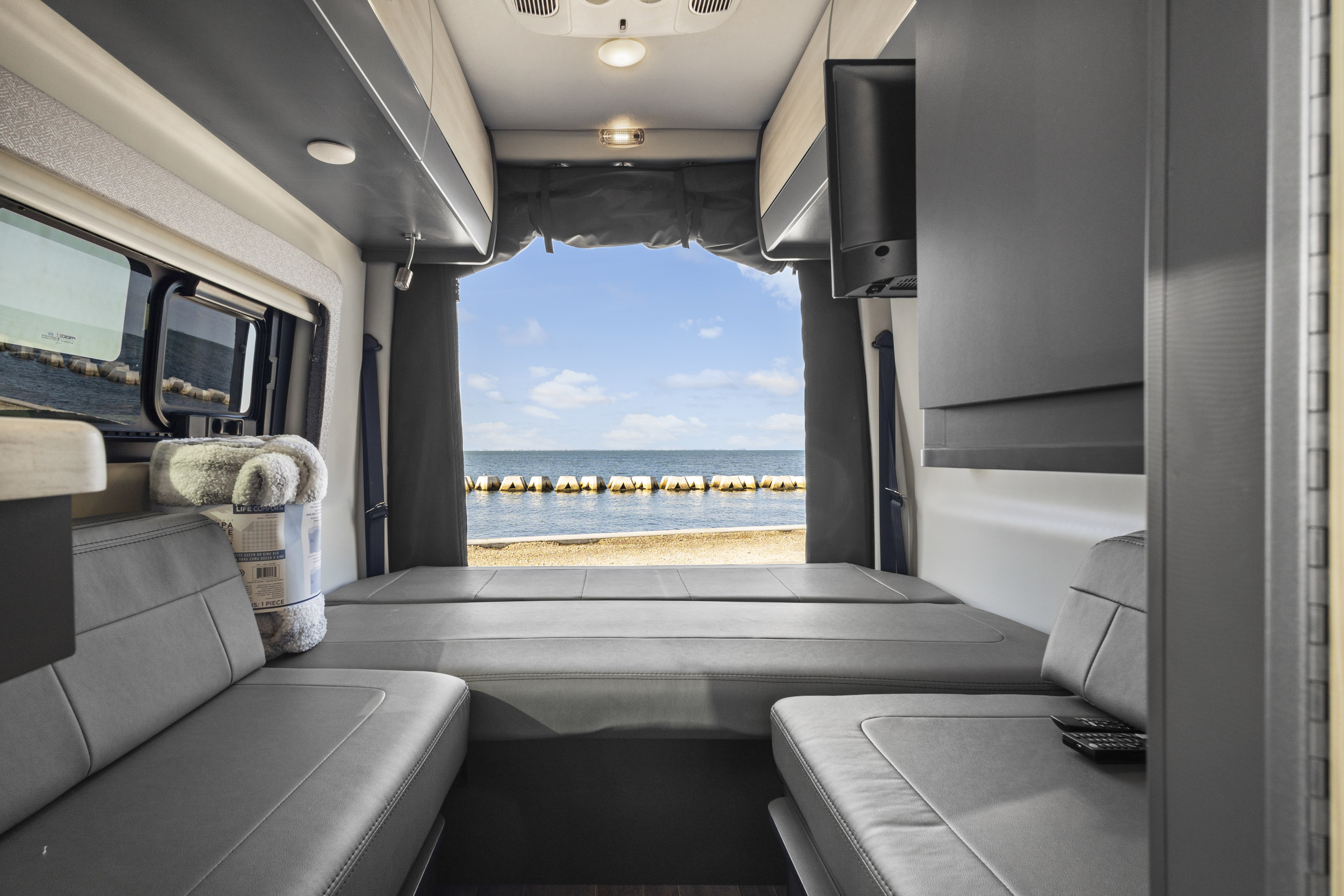 Cozy rv rental interior with plush grey beds and a stunning ocean view. Perfect for serene beachside adventures.. Thor Sanctuary 2023