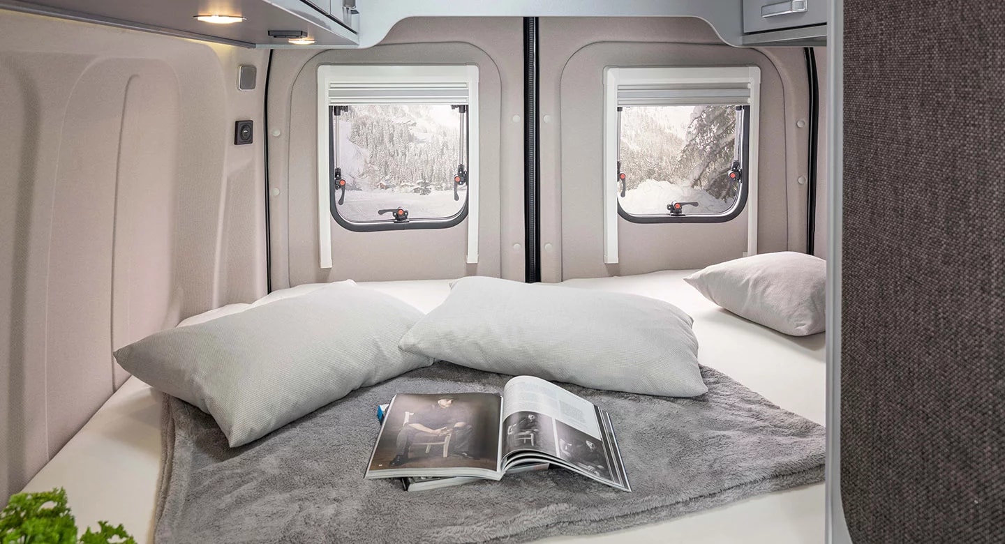 Cozy rv rental bedroom setup with a comfy bed, pillows, and windows showcasing a snowy forest. Ideal for winter adventures.. weinsberg 550 2024