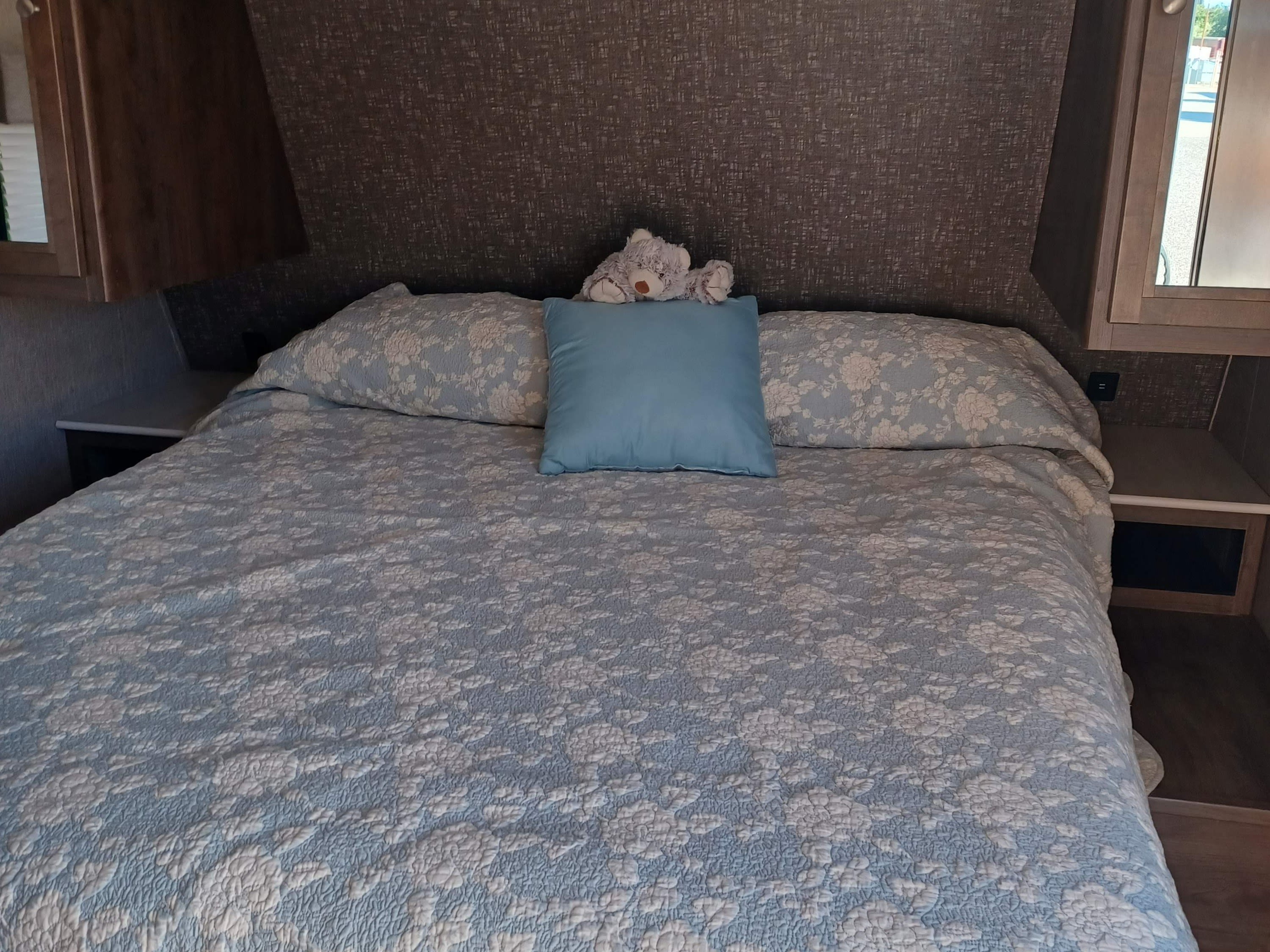 Cozy RV rental bedroom featuring a comfortable bed with a light blue patterned comforter, pillows, and a teddy bear.. Dutchmen Coleman Lantern LT 2020