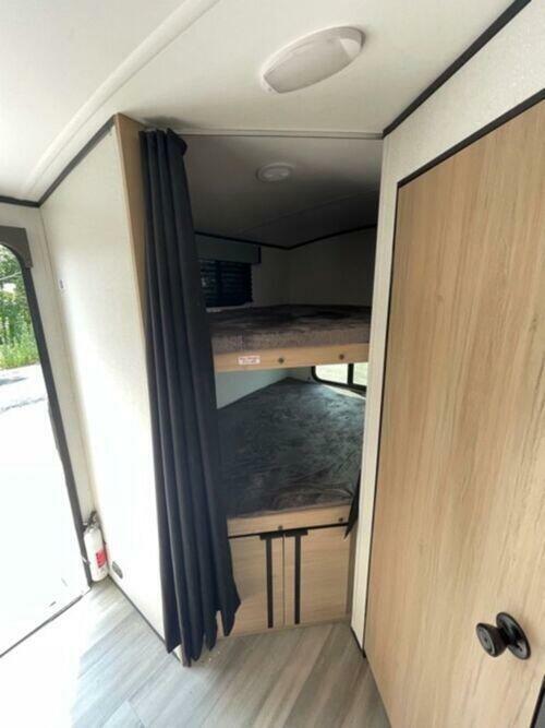 RV rental interior: Bunk beds with privacy curtain, a fire extinguisher near the open doorway, and wood-look flooring.. Cruiser Rv Corp Radiance 2022
