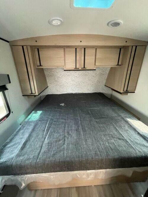 Spacious RV rental bedroom featuring a large bed, overhead cabinets, and bright window for comfortable travel.. Cruiser Rv Corp Radiance 2022