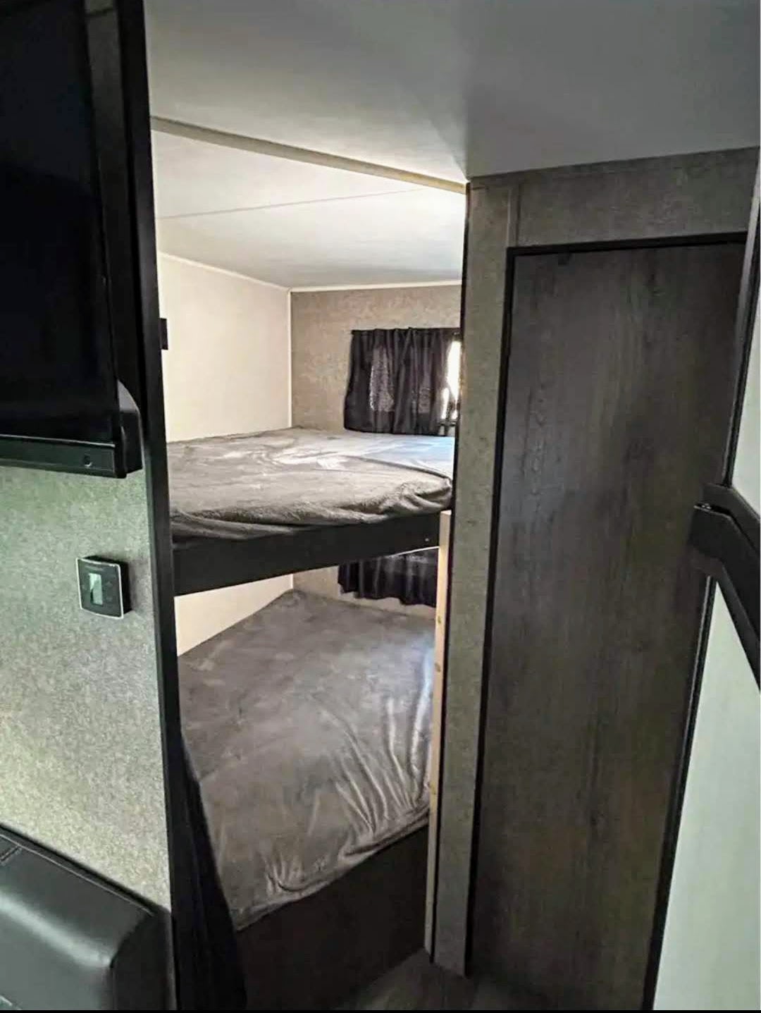 Cozy RV rental bunk beds, perfect for family travel. Features window, partial TV, and comfortable gray bedding.. Highland Ridge RV Open Range 2021