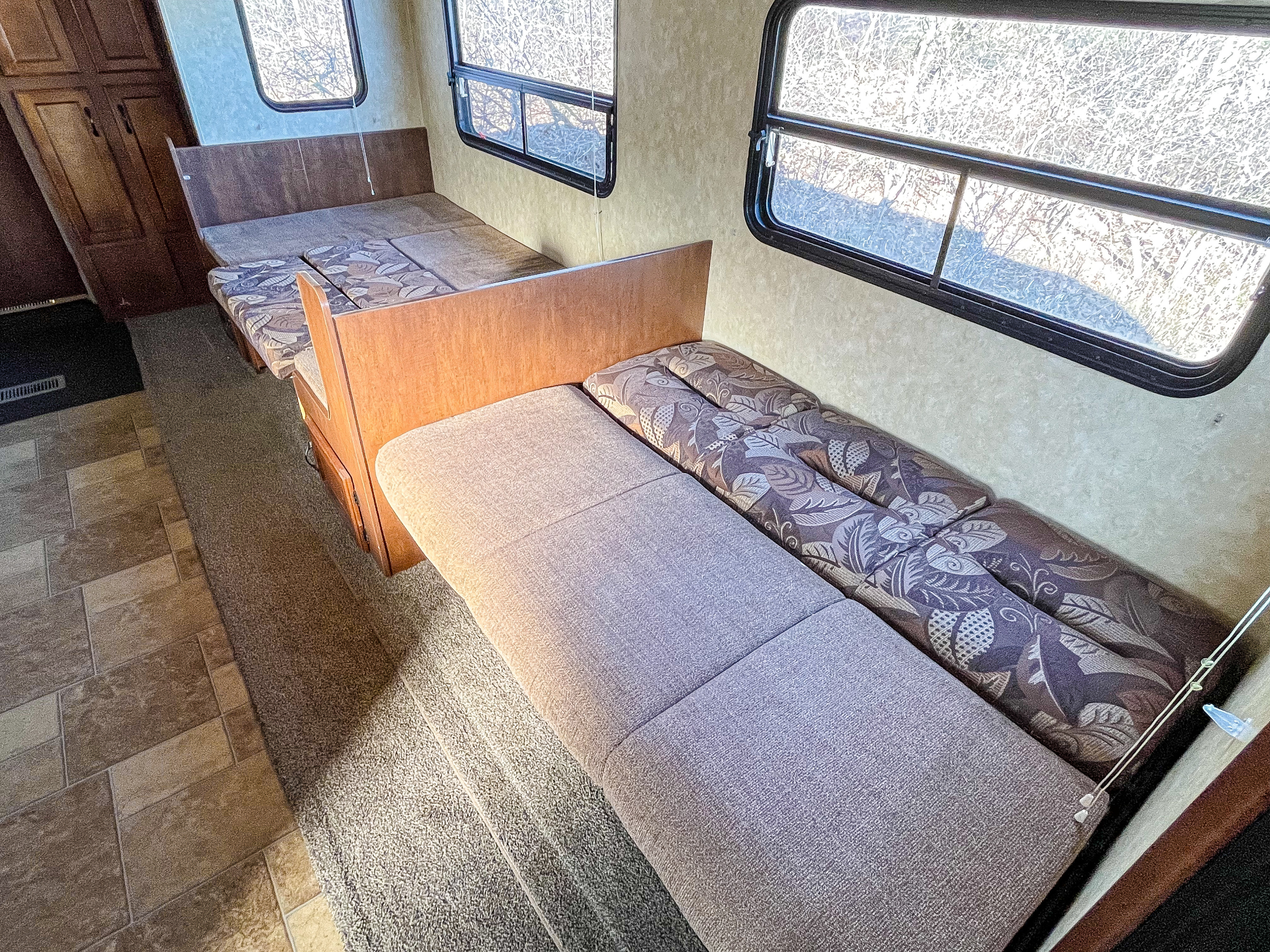 An RV rental's interior, featuring two bench seats with patterned and solid cushions, windows, and mixed flooring.. Coachmen Catalina 2013