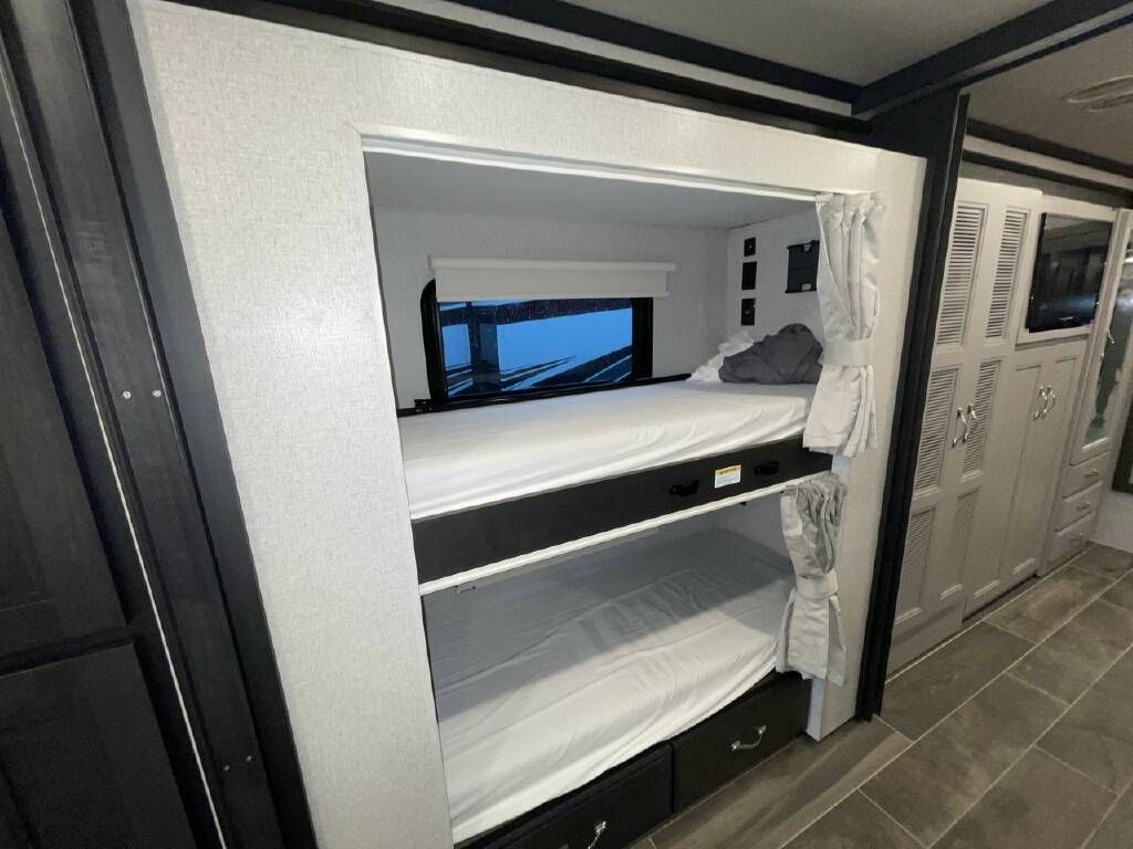 RV rental: Compact bunk beds with window, white sheets, and adjacent storage create a functional sleeping area.. Thor Motor Coach Venetian 2024