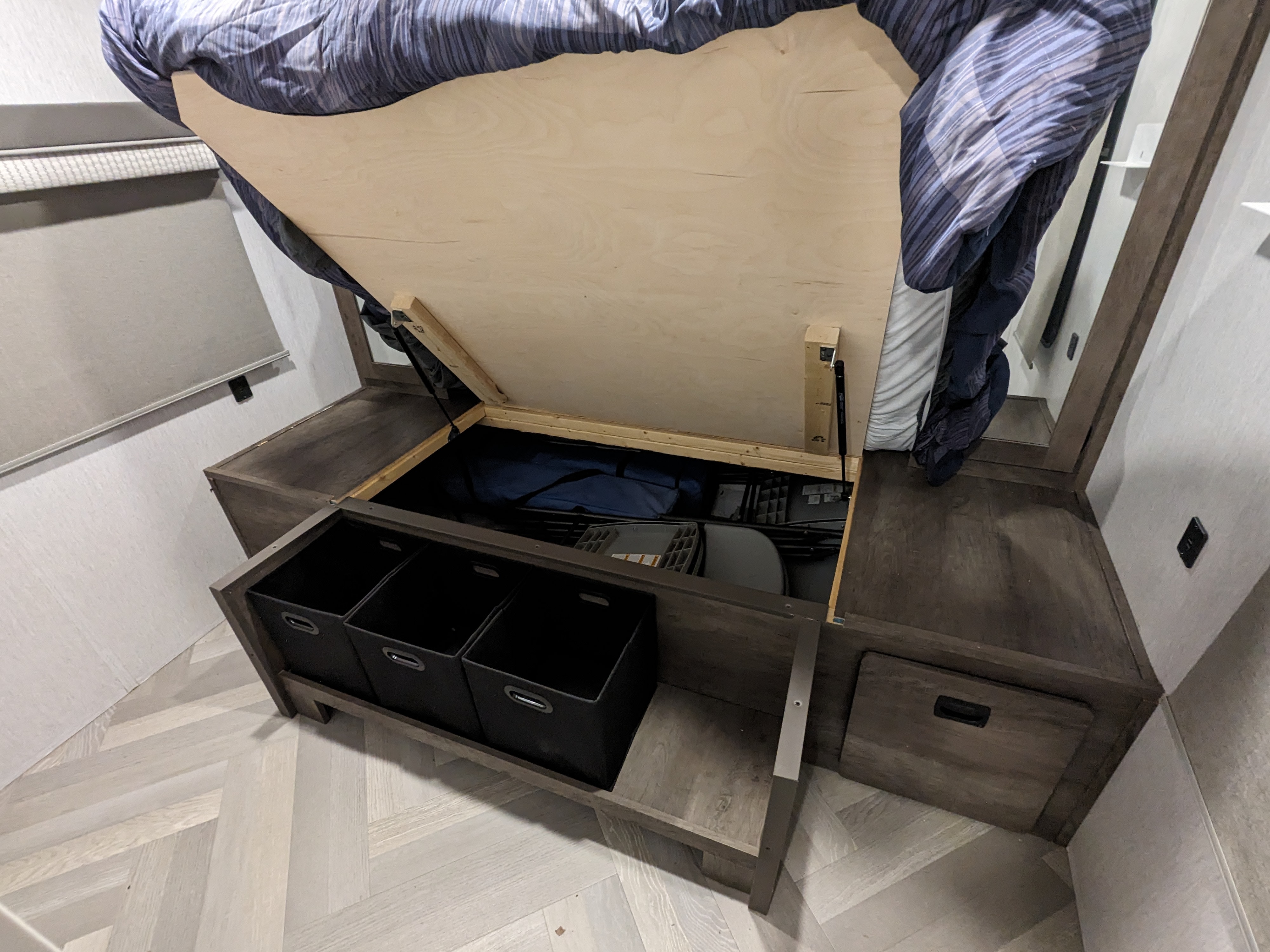 This RV rental bed lifts for hidden storage, revealing a blue bag, folded chairs, and pull-out bins for organization.. Forest River Salem Cruise Lite 2022