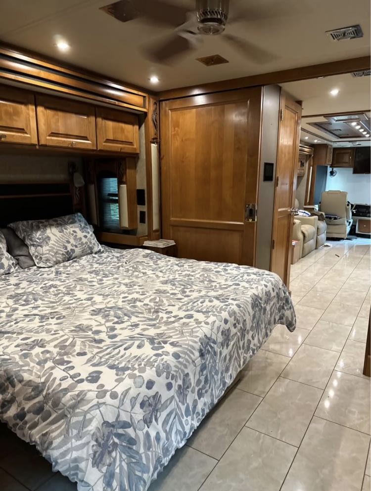Spacious RV rental interior: bedroom with patterned bedding, wood cabinets, and tile floor extending to living area.. Tiffin Motorhomes Phaeton 2019