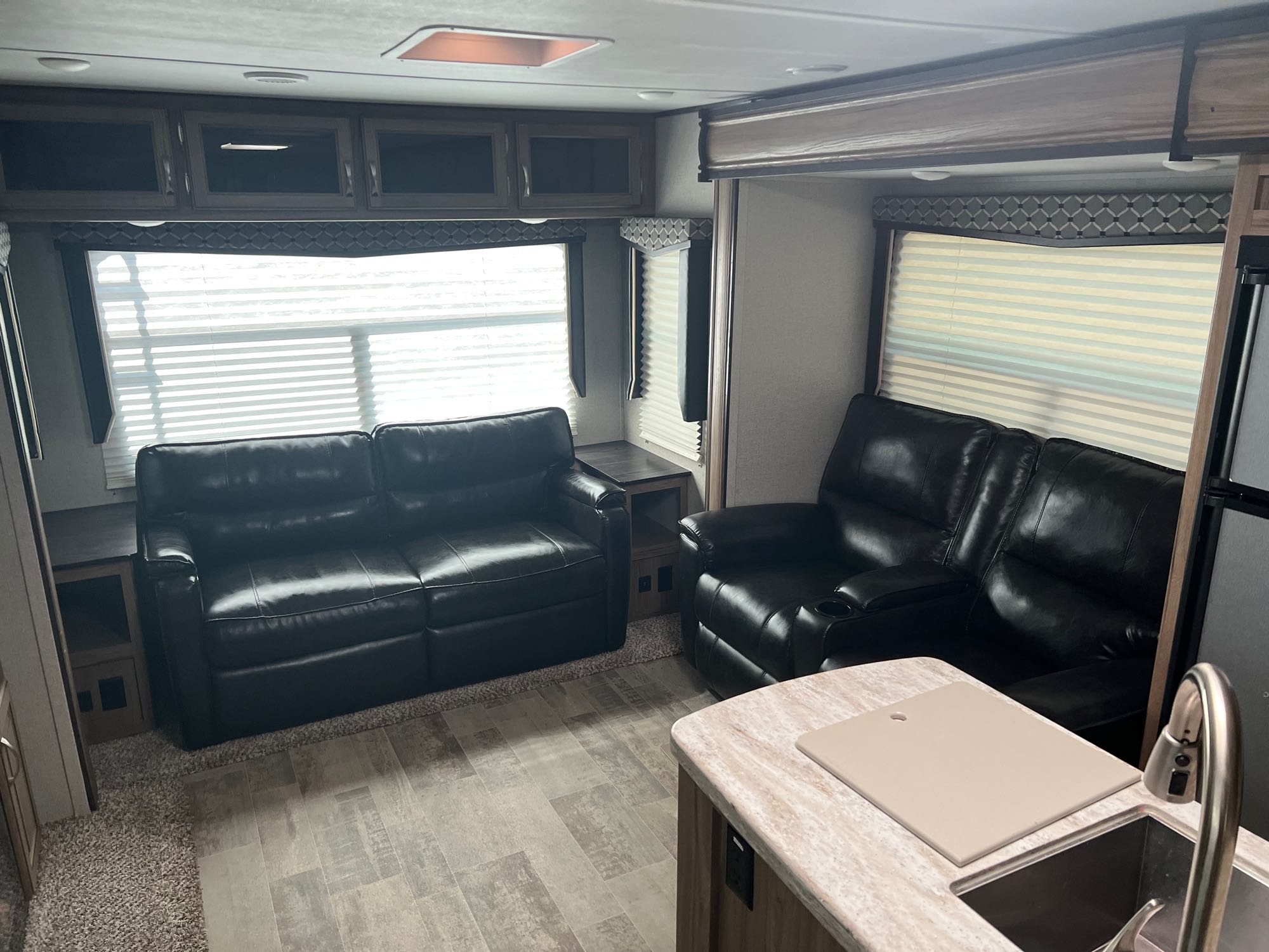 Comfortable RV rental living space with black leather sofas, kitchen counter, and overhead storage cabinets.. Atlas Atlas Trailer 2019