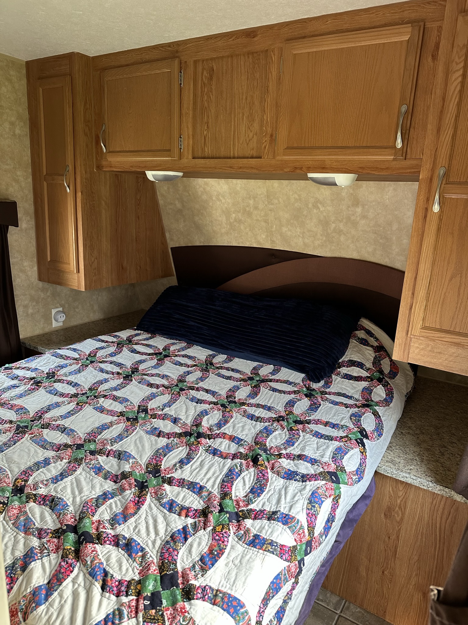 RV rental bedroom with a colorful wedding ring quilt on the bed, flanked by wood overhead cabinets and a built-in headboard.. Jayco Jay Flight 2009