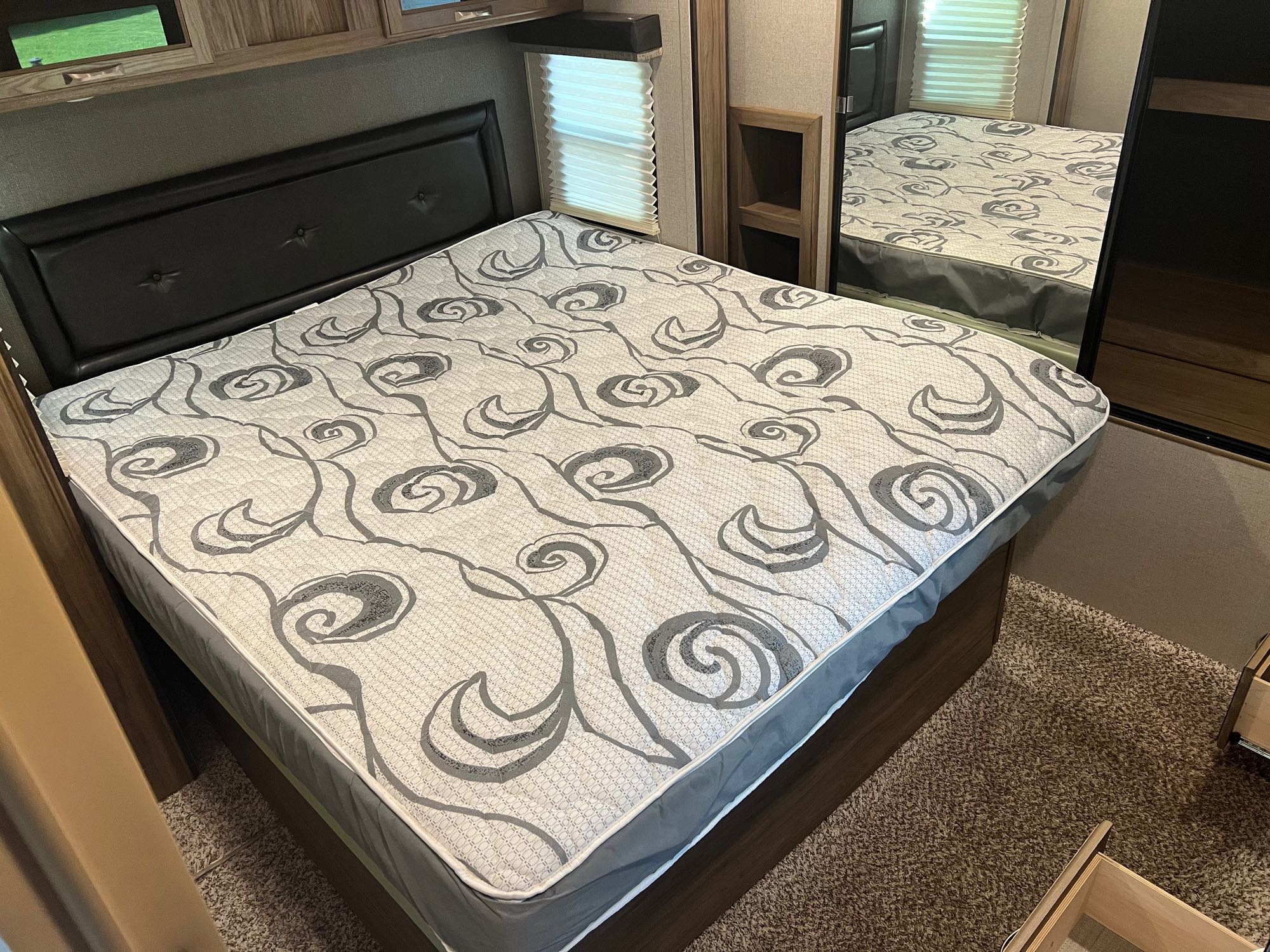 RV rental bedroom: a cozy bed with a patterned mattress, black headboard, window blind, and mirror in the interior.. Atlas Atlas Trailer 2019