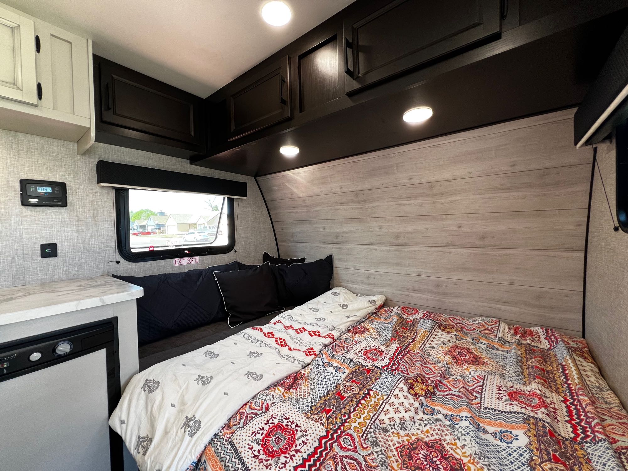Cozy RV rental interior: A modern bedroom with a colorful quilt, dark overhead cabinets, and a mini-fridge.. Jayco Jay Flight SLX Baja Edition 2023