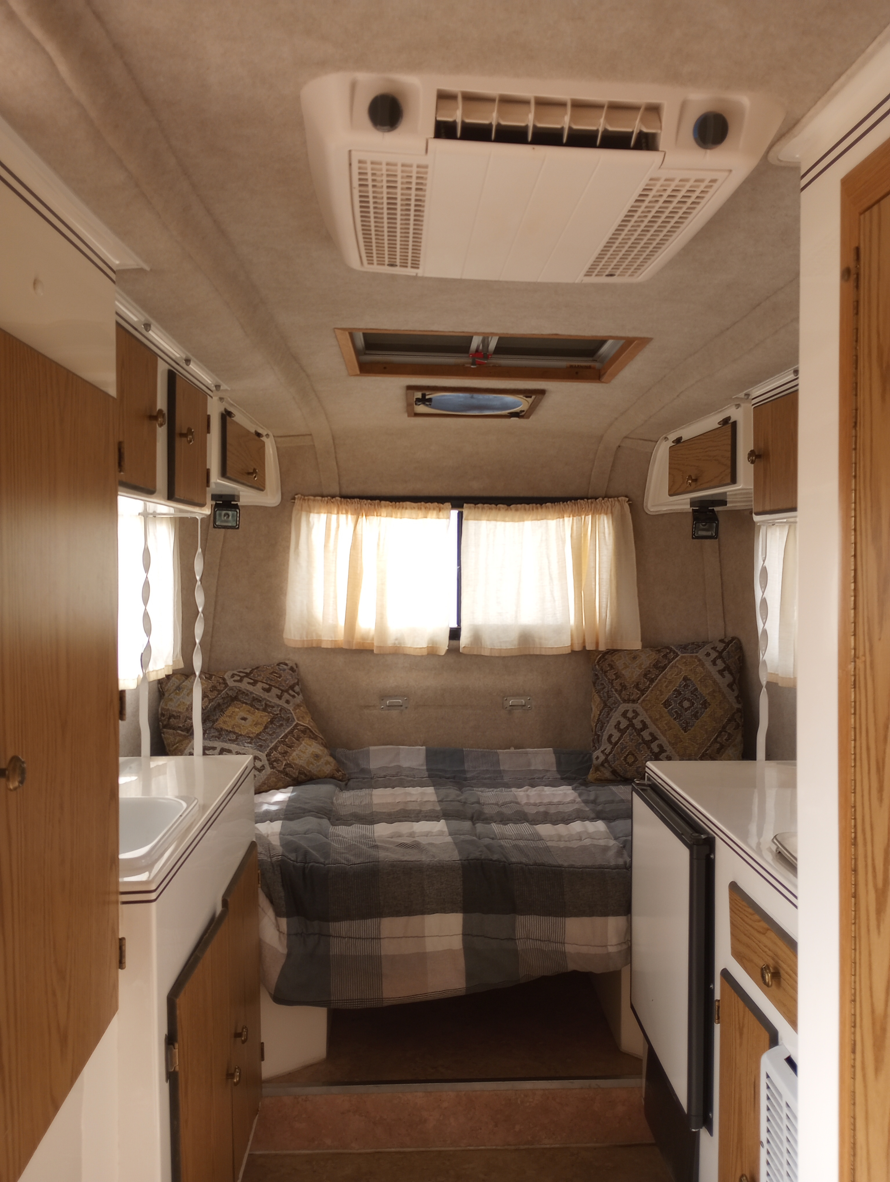 Interior view of a clean RV rental, featuring a bed, small kitchen, overhead cabinets, and air conditioning.. Scamp Scamp Trailer 2011