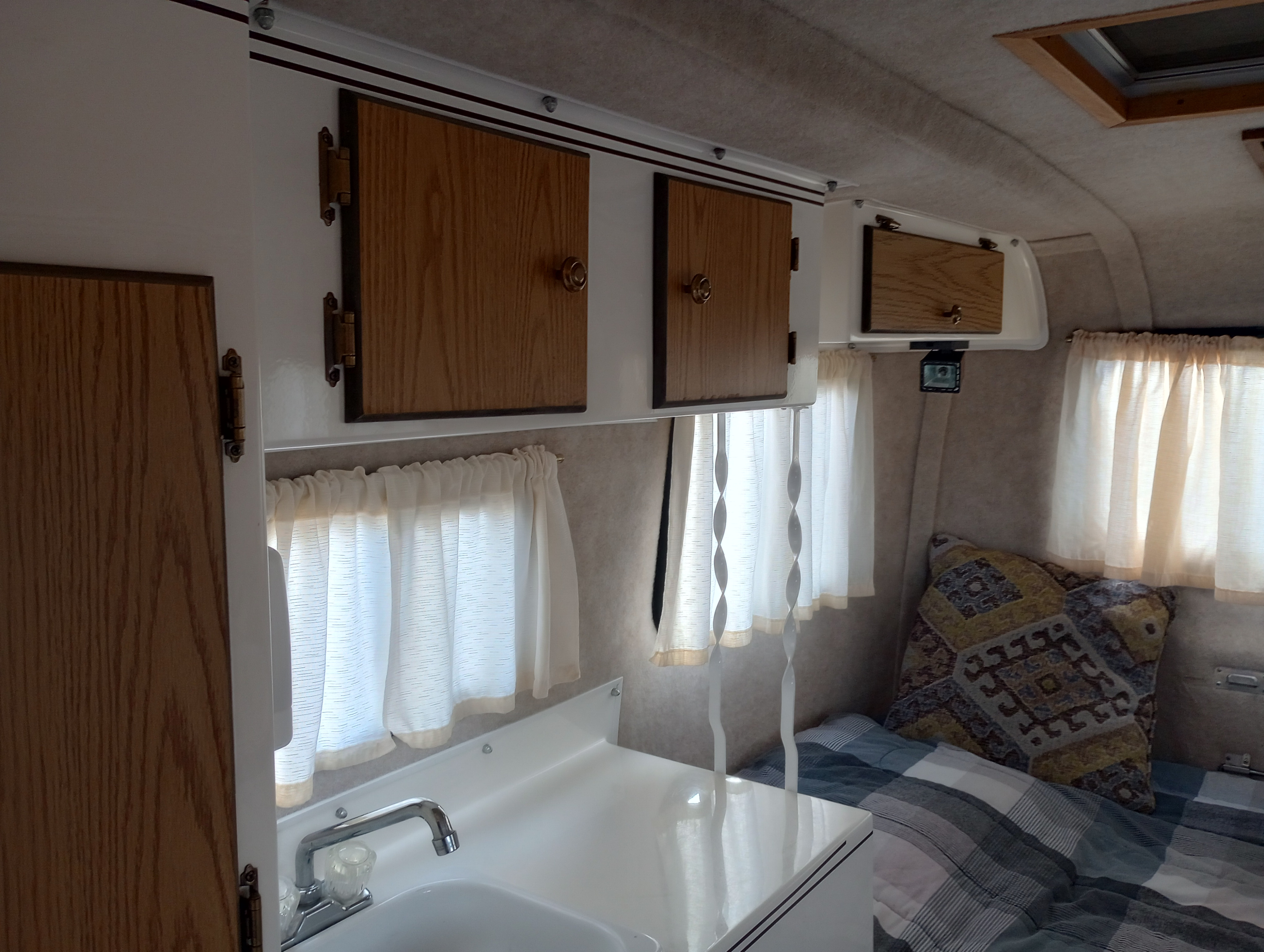 Inside a cozy RV rental: compact kitchen with sink, wooden cabinets, and a comfortable sleeping area. Ideal for road trips.. Scamp Scamp Trailer 2011