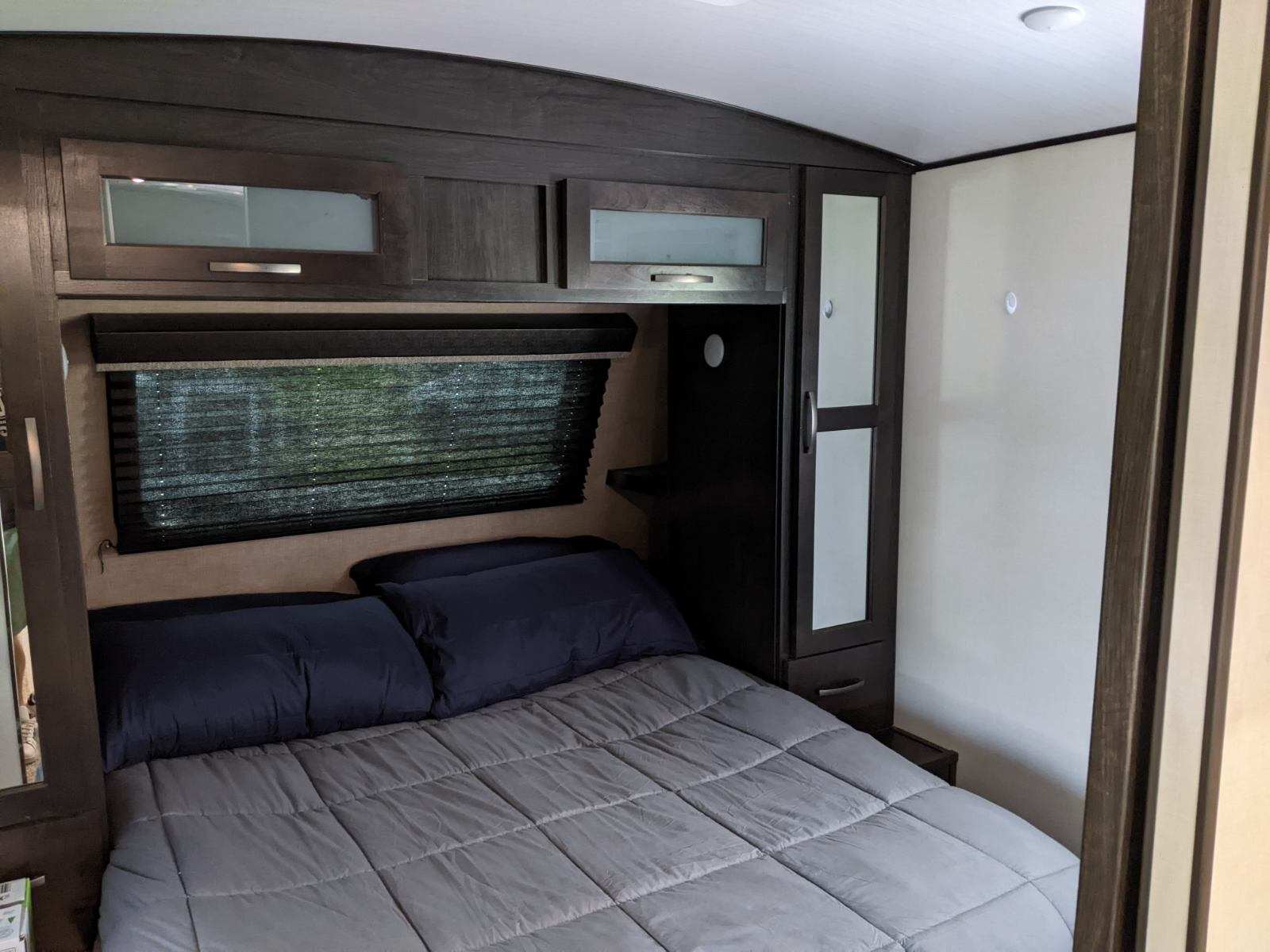 Cozy RV rental bedroom with a comfortable bed, overhead cabinets, and window blinds.. Grand Design Transcend Xplor 2021