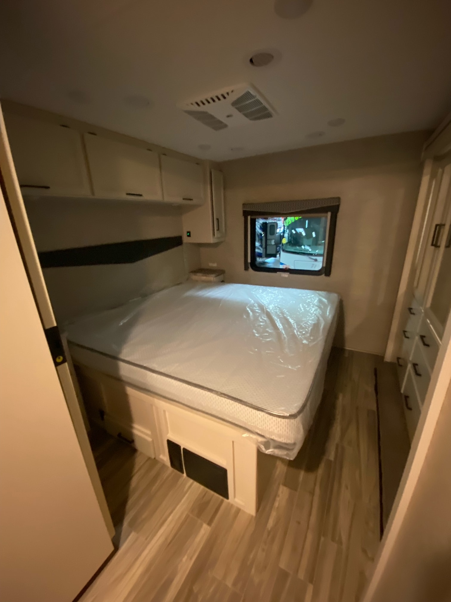RV rental bedroom interior, showing a plastic-covered mattress on bed frame, wall cabinets, and a side window. Compact and ready for use.. Thor Windsport 2022