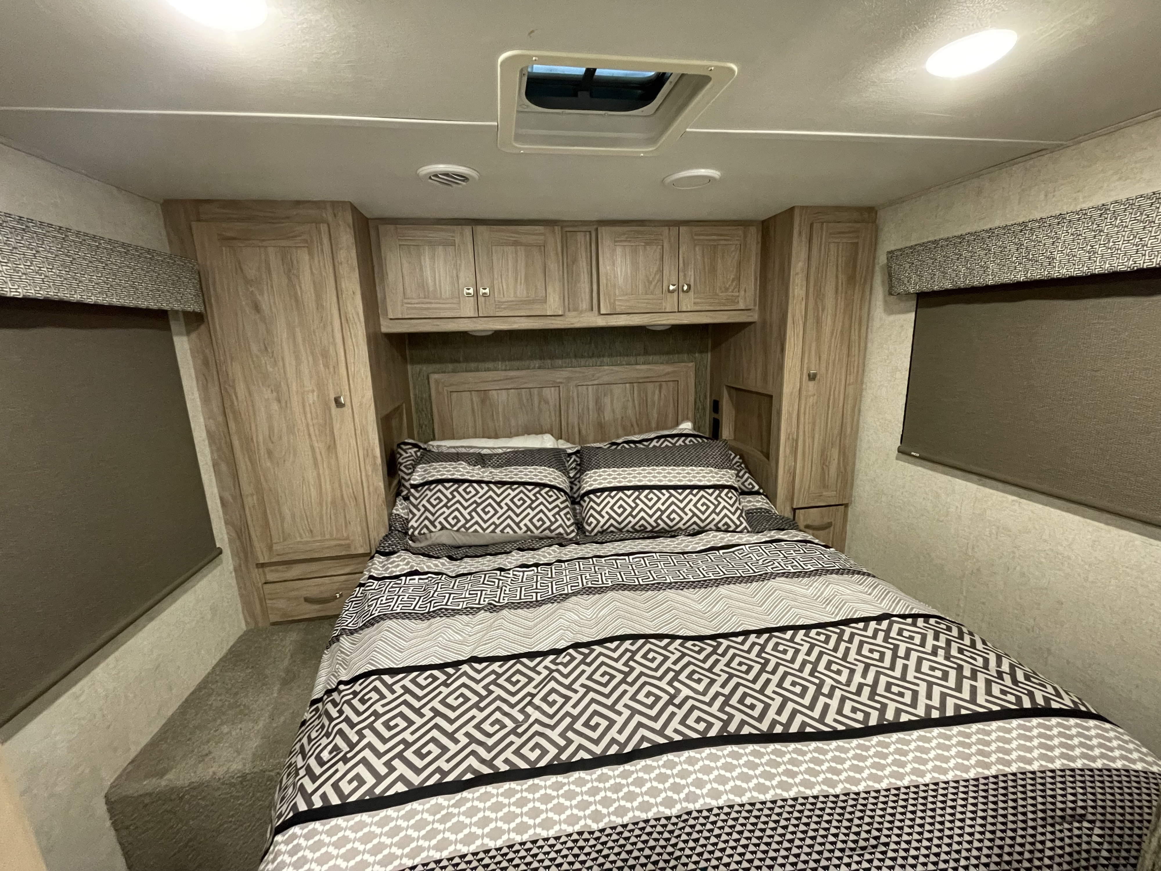 Cozy RV rental bedroom featuring a full bed with patterned bedding, overhead cabinets, wardrobes, and a window for comfortable stays.. Forest River Sunseeker 2018