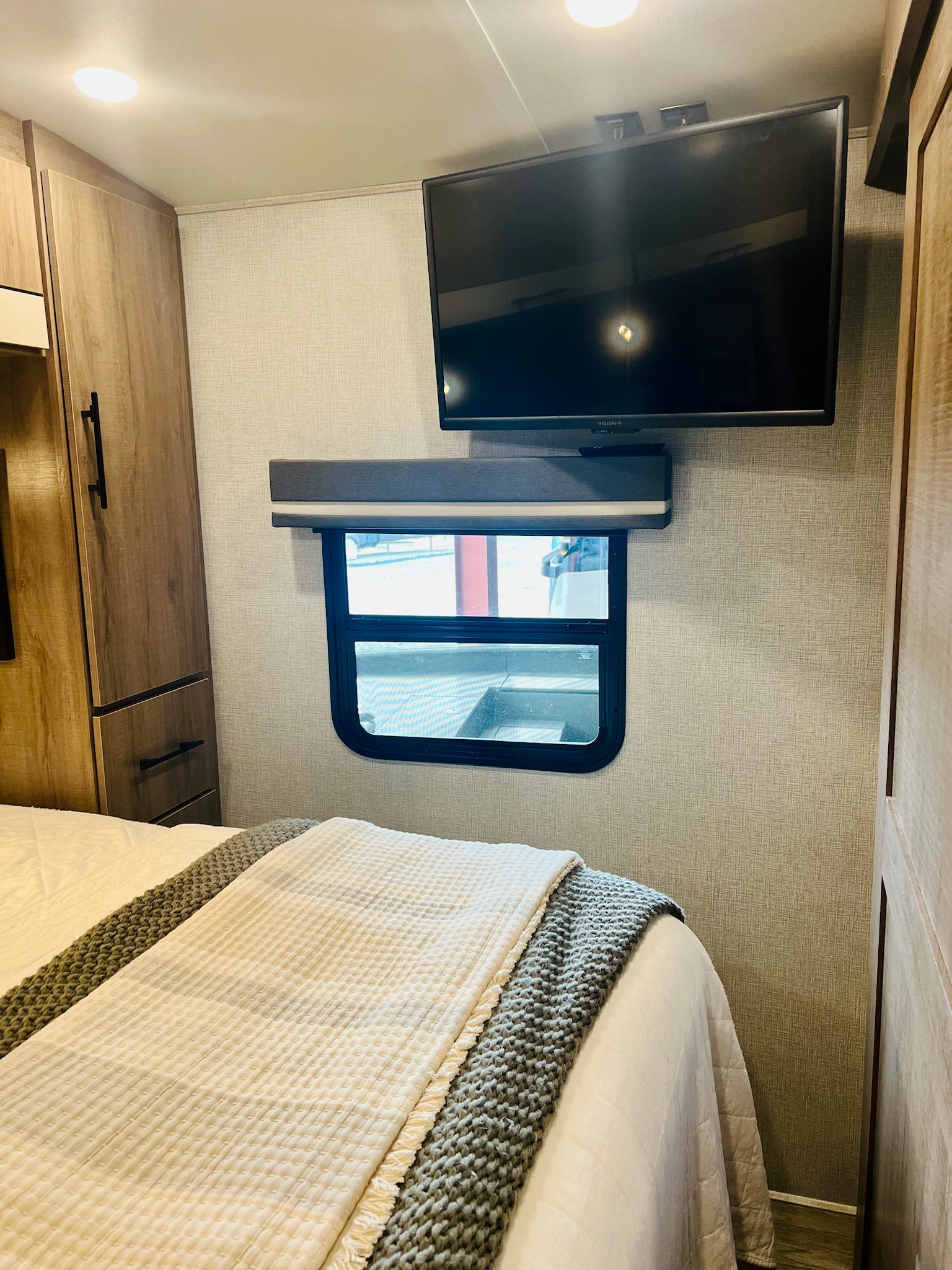 Cozy RV rental bedroom with a comfy bed, wall-mounted TV, window, and wood cabinets. Perfect for your travels!. Grand Design Imagine 2023