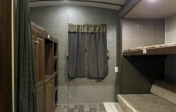 RV rental interior: bunkhouse with beds, a storage cabinet, and window with patterned curtains, offering comfy sleeping.. Keystone RV Bullet Premier 2016