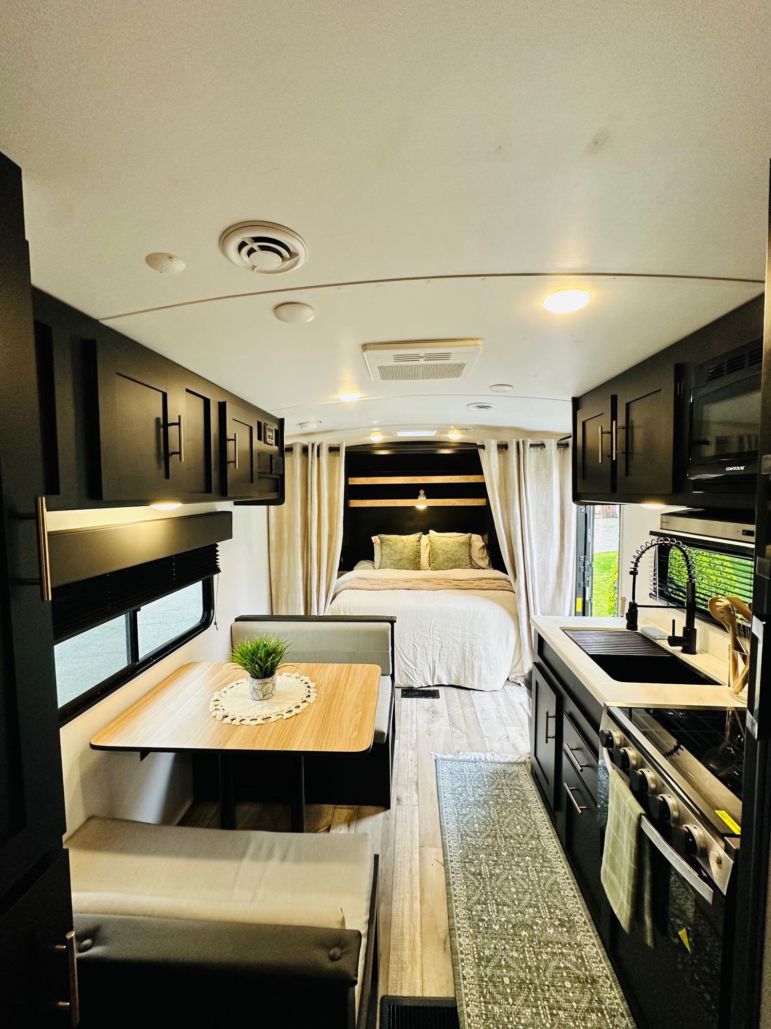 Modern RV rental interior showing a compact kitchen, dinette with seating, and a comfortable bed area with privacy curtains.. Keystone RV Springdale 2023