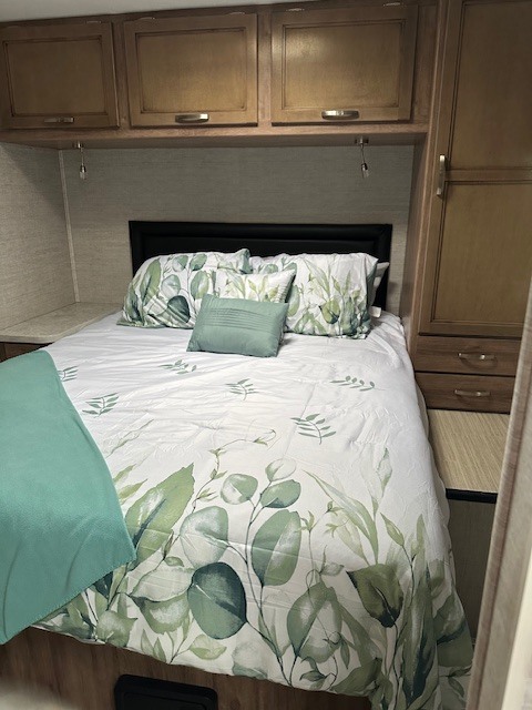 Cozy RV rental bedroom with nature-themed bedding, a comfortable bed, and wood overhead cabinets.. Jayco Redhawk SE 2021