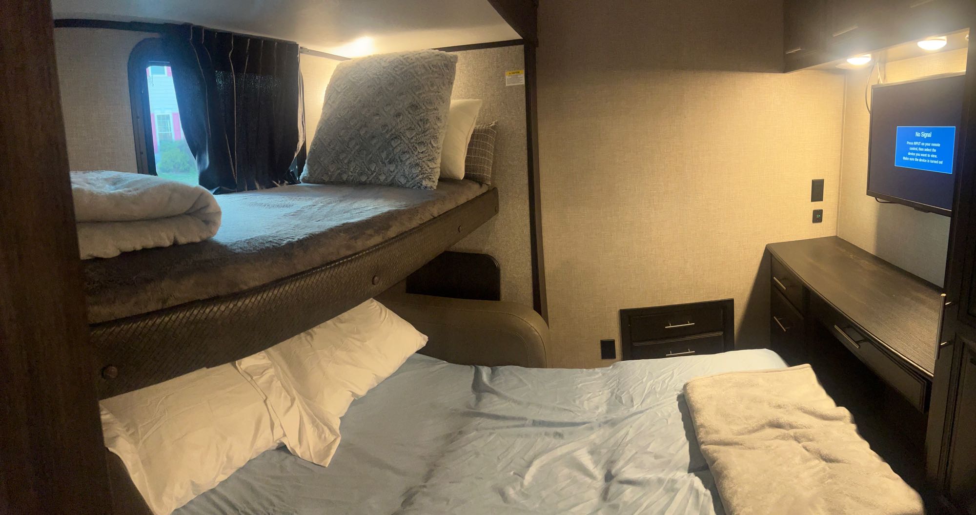 Cozy RV rental interior shows bunk beds with bedding, a functional desk area, and a wall-mounted TV.. Jayco North Point 2022